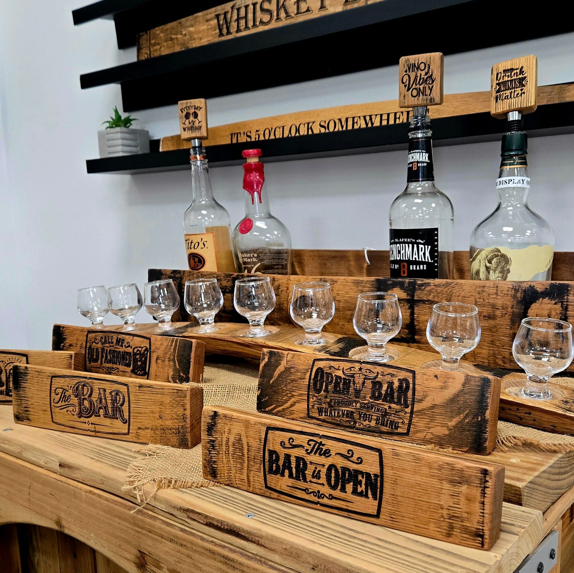 Wooden bar signs and bottles on a wooden table with glasses, shelves with signs in the background.
