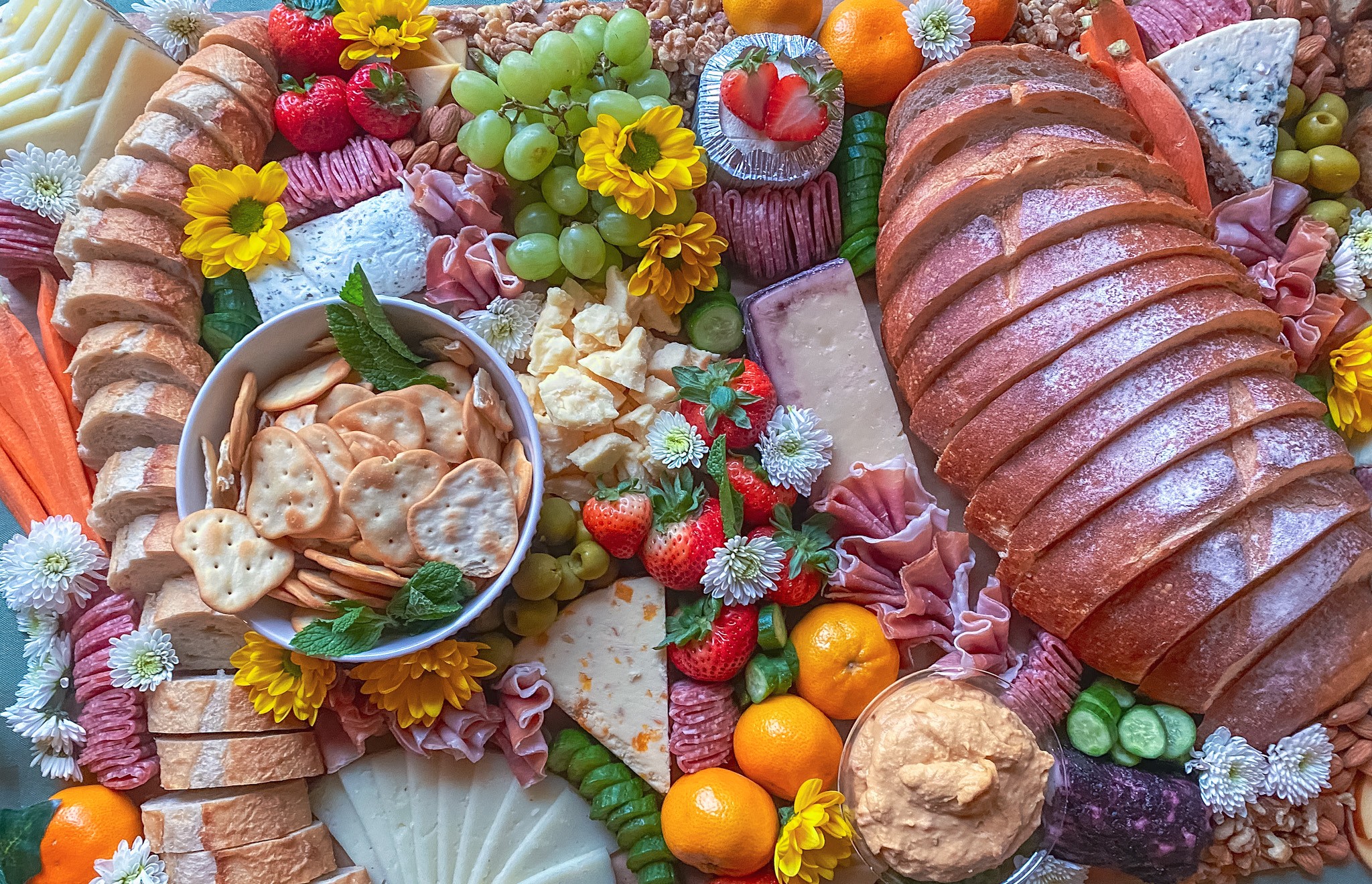 Assorted meats, cheeses, fruits, and flowers arranged on a platter with various colorful garnishes.