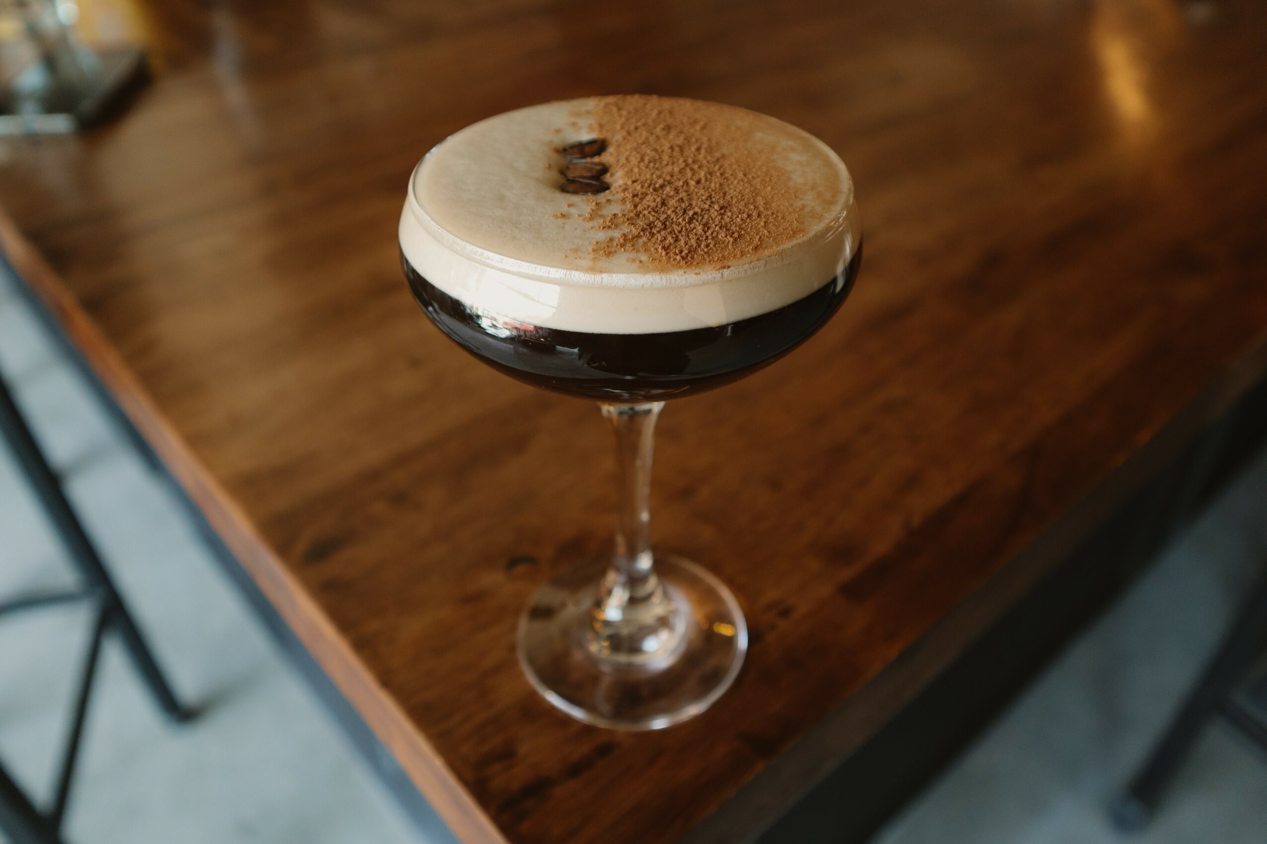 Coffee cocktail with foam and cocoa powder in a glass on a wooden table.