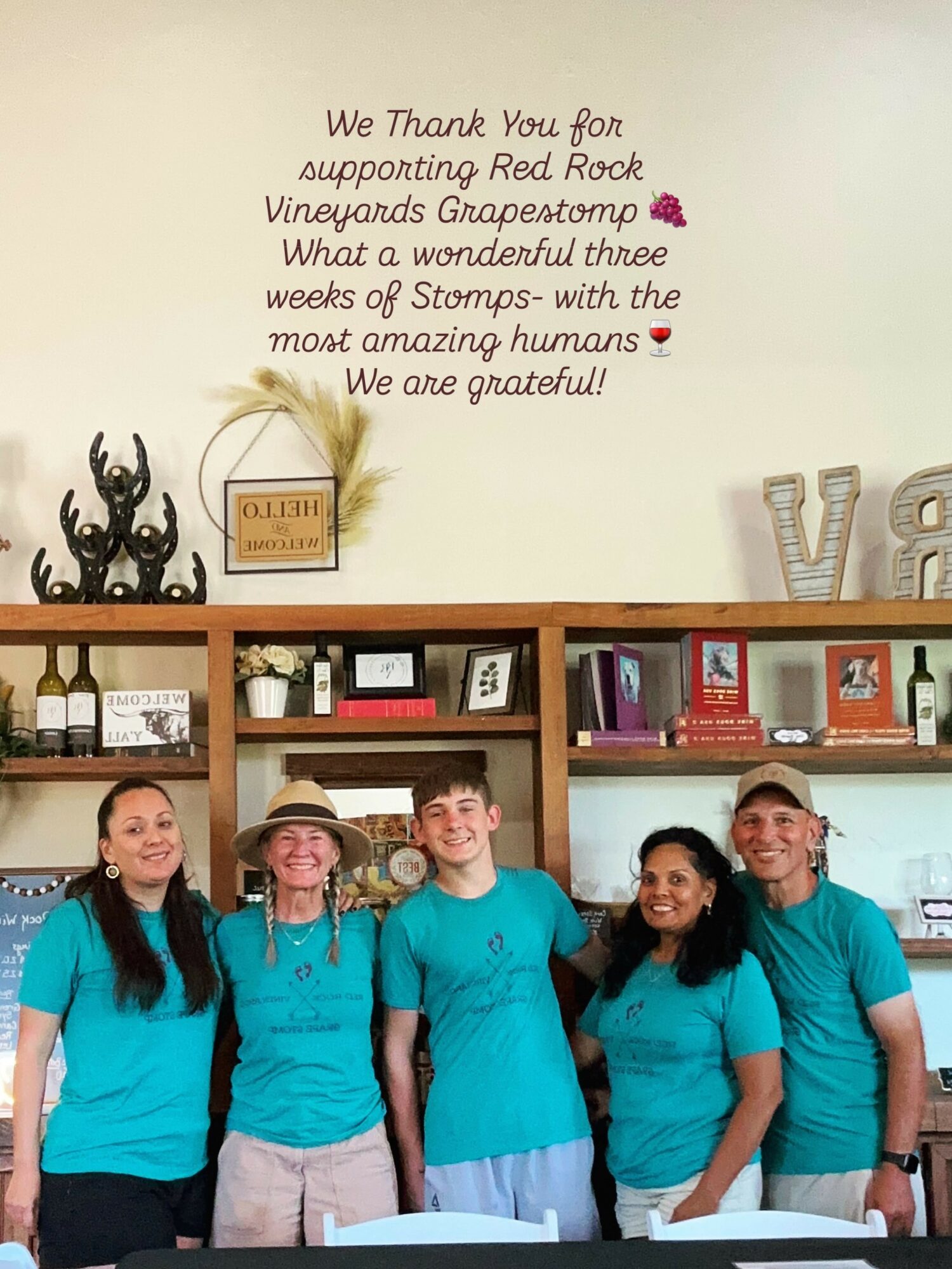 Five people wearing teal shirts stand in front of shelves with books and decorations, smiling at the camera.