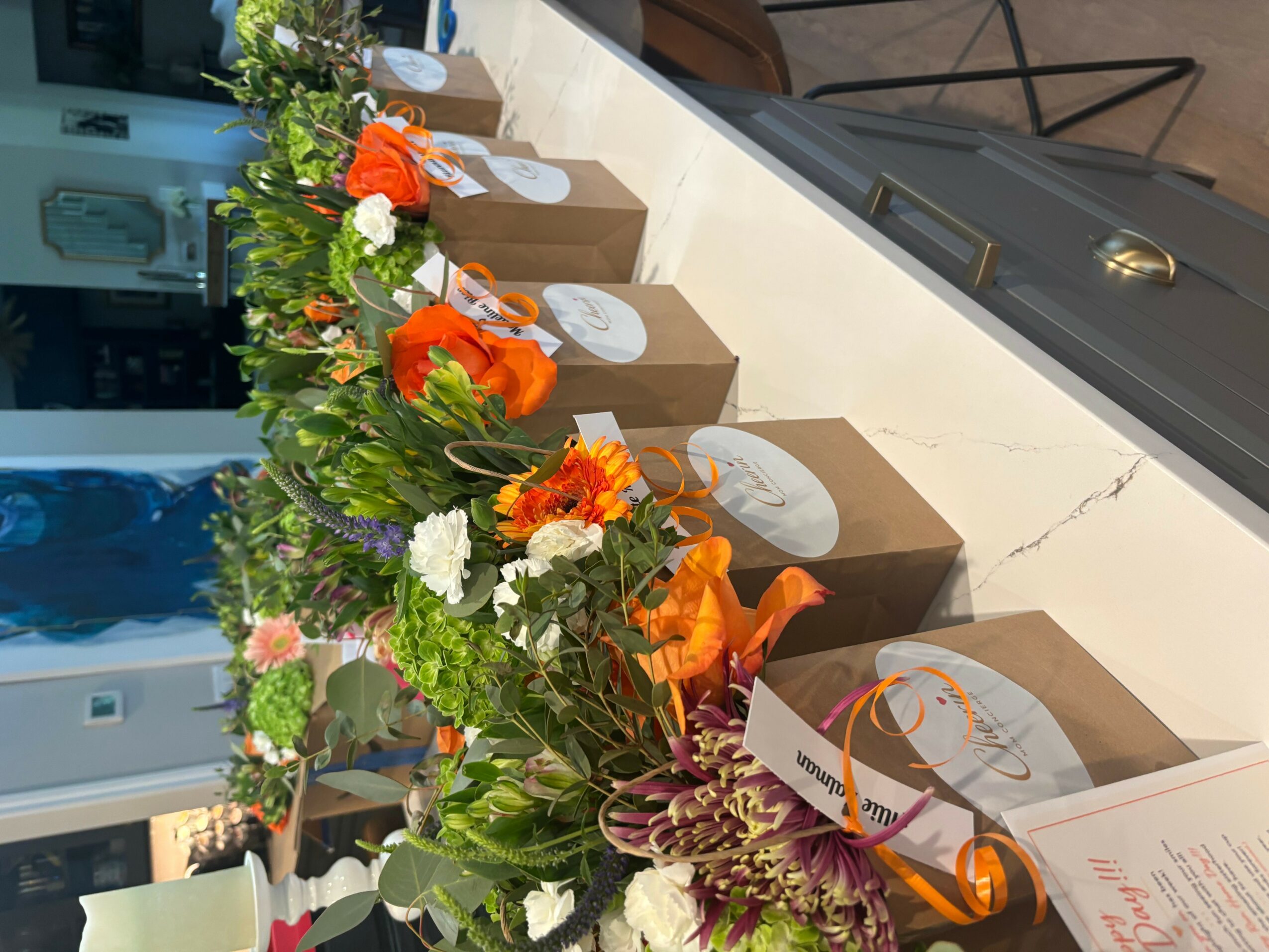Long table with flower arrangements and wrapped gifts, set for a celebration or event, indoors.