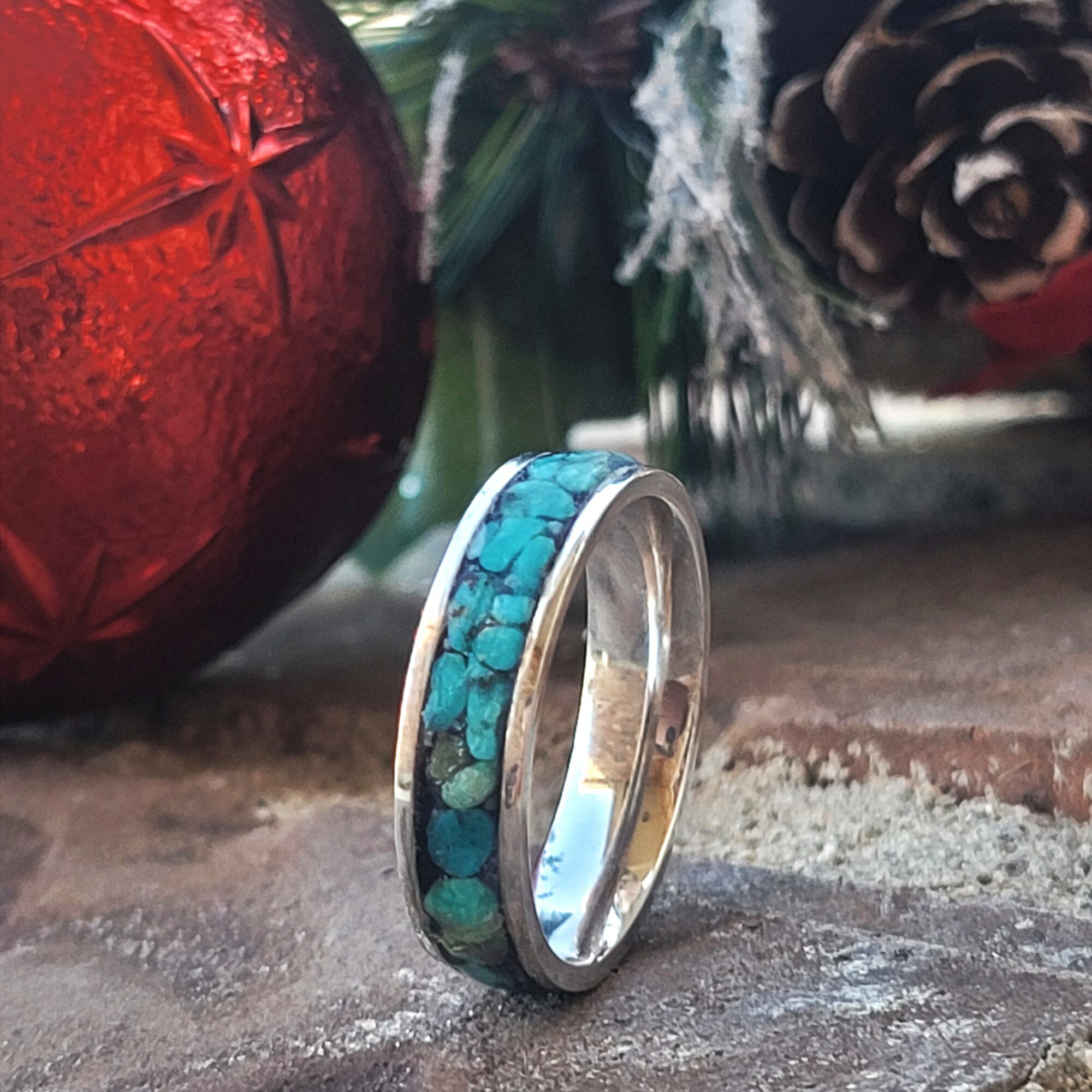 Ring with turquoise inlay on a wooden surface, with Christmas decorations in the background.