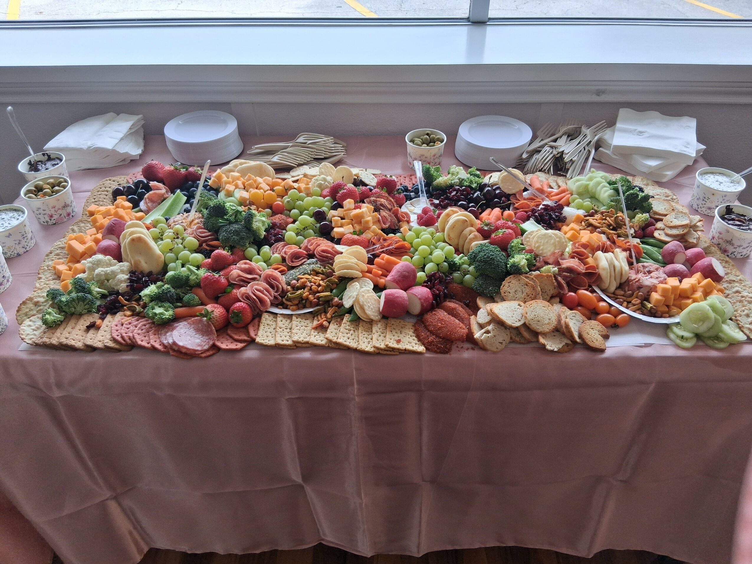 Fruit and snack platter with grapes, strawberries, cookies, and cheese on a table, with bowls and napkins in the background.