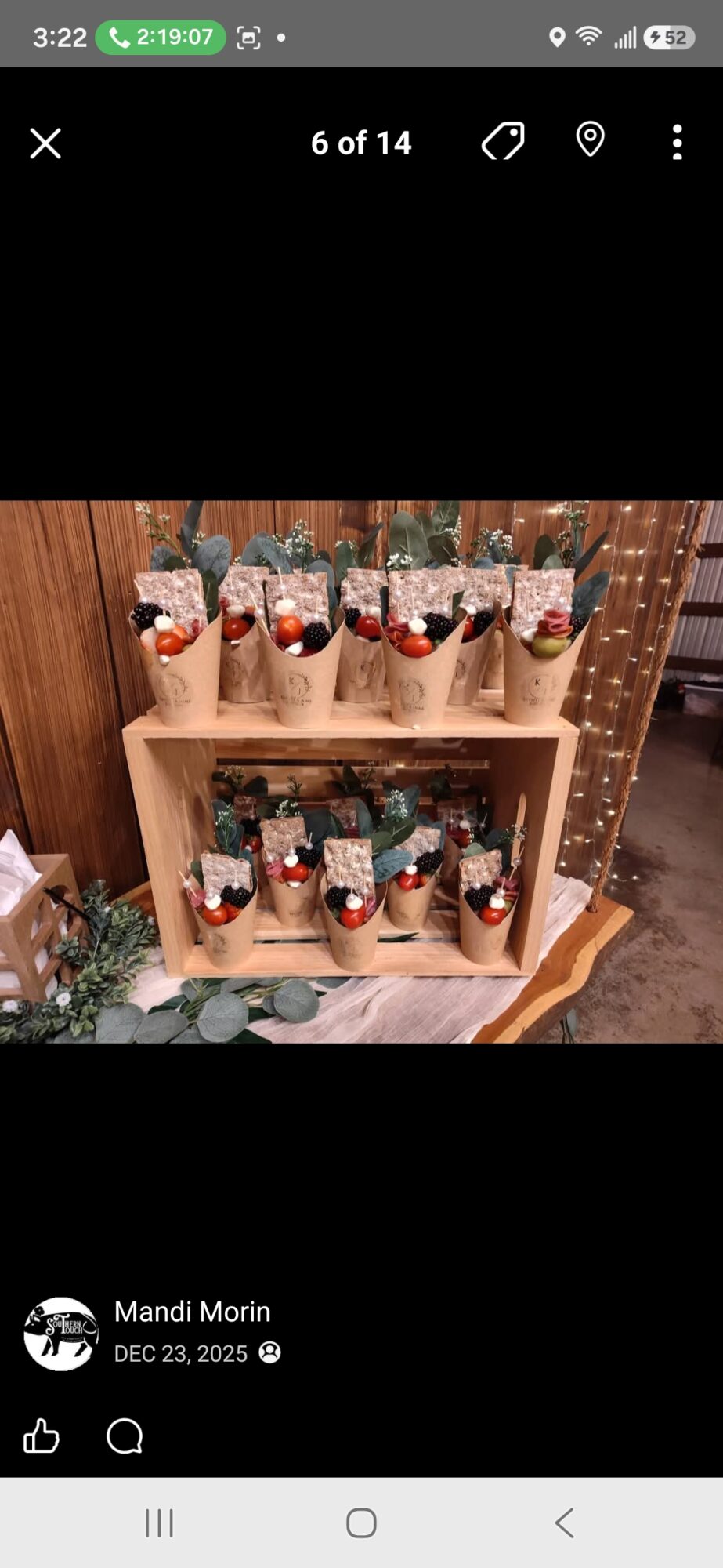 Display of small gift bags with red and white decorations on a wooden shelf, decorated with greenery and fairy lights.