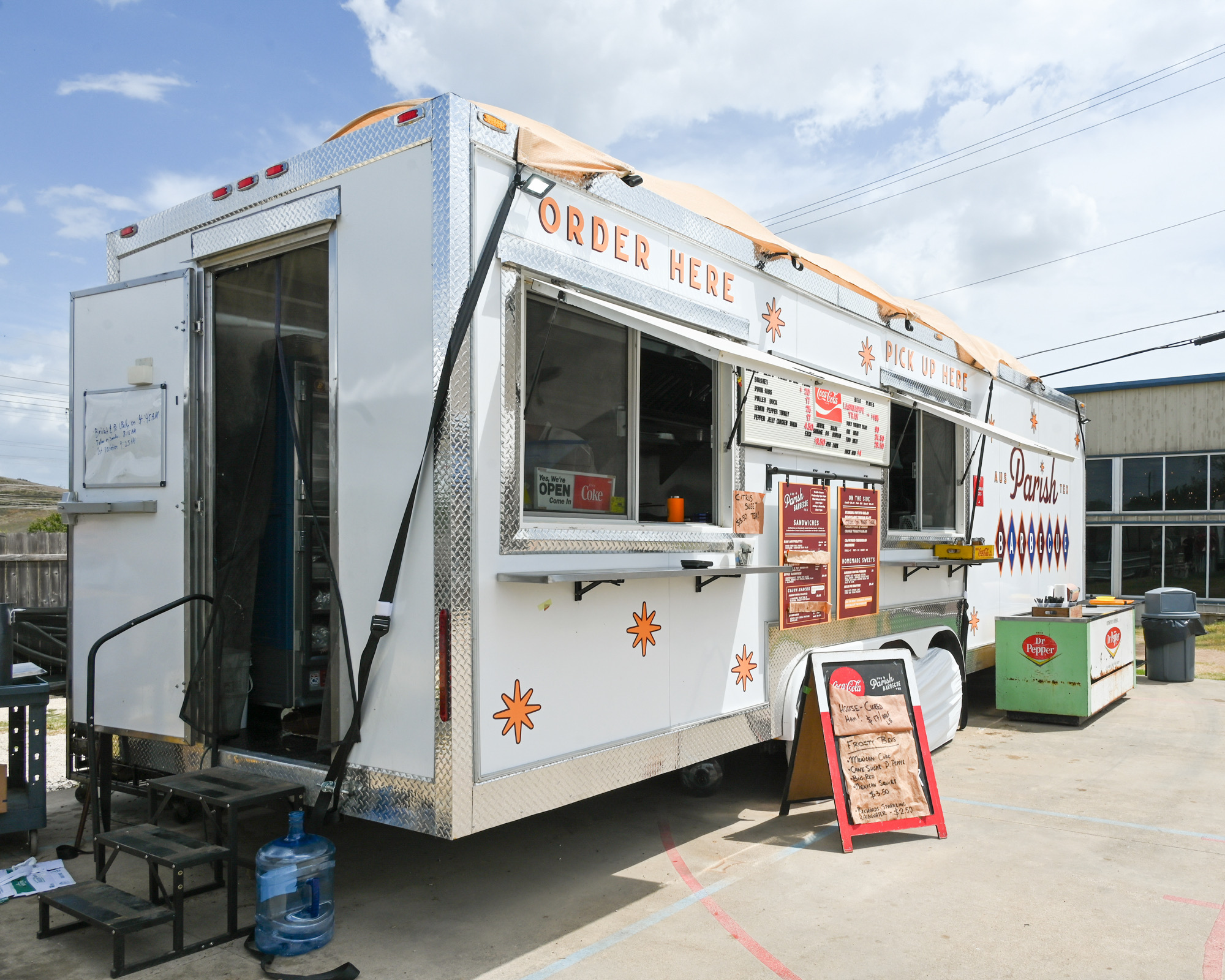 Food truck with menu boards and a service window, parked outdoors on a sunny day.