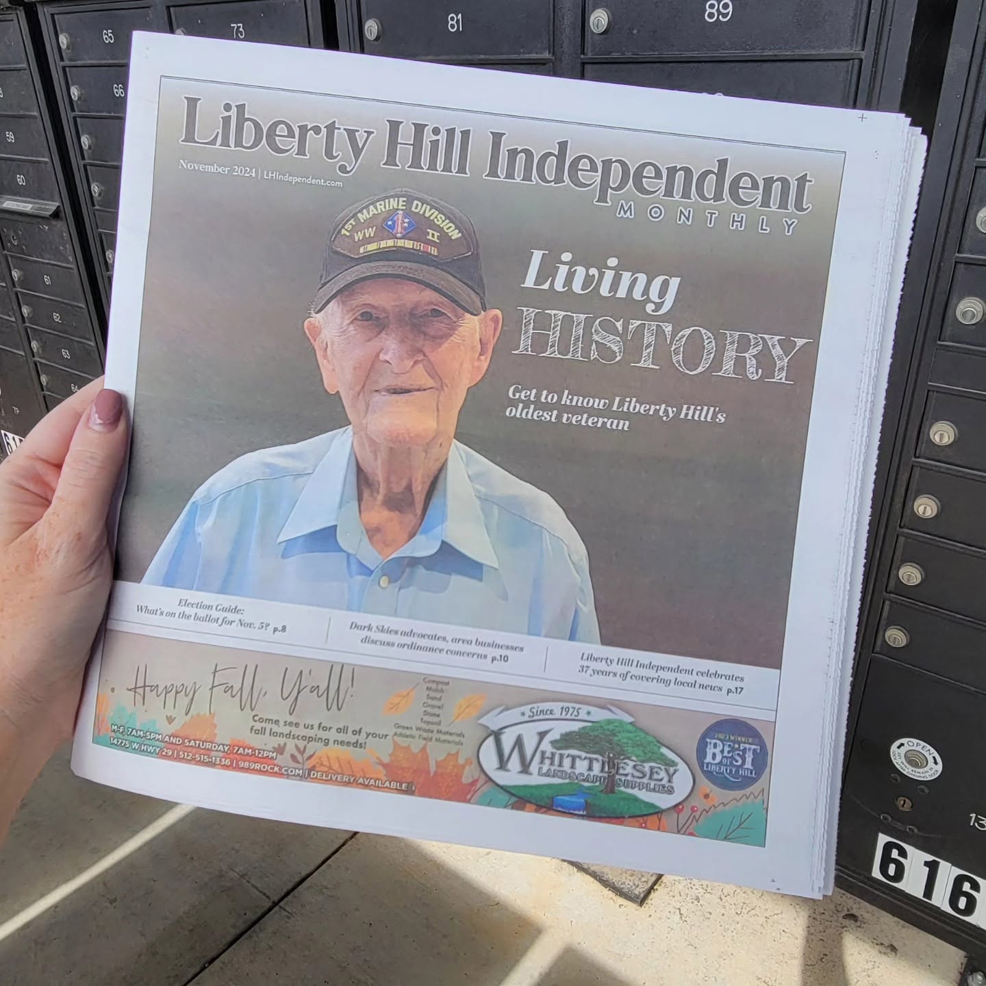 Person holding a newspaper with a photo of an elderly man wearing a cap and blue shirt, headline reads 'Living History'.