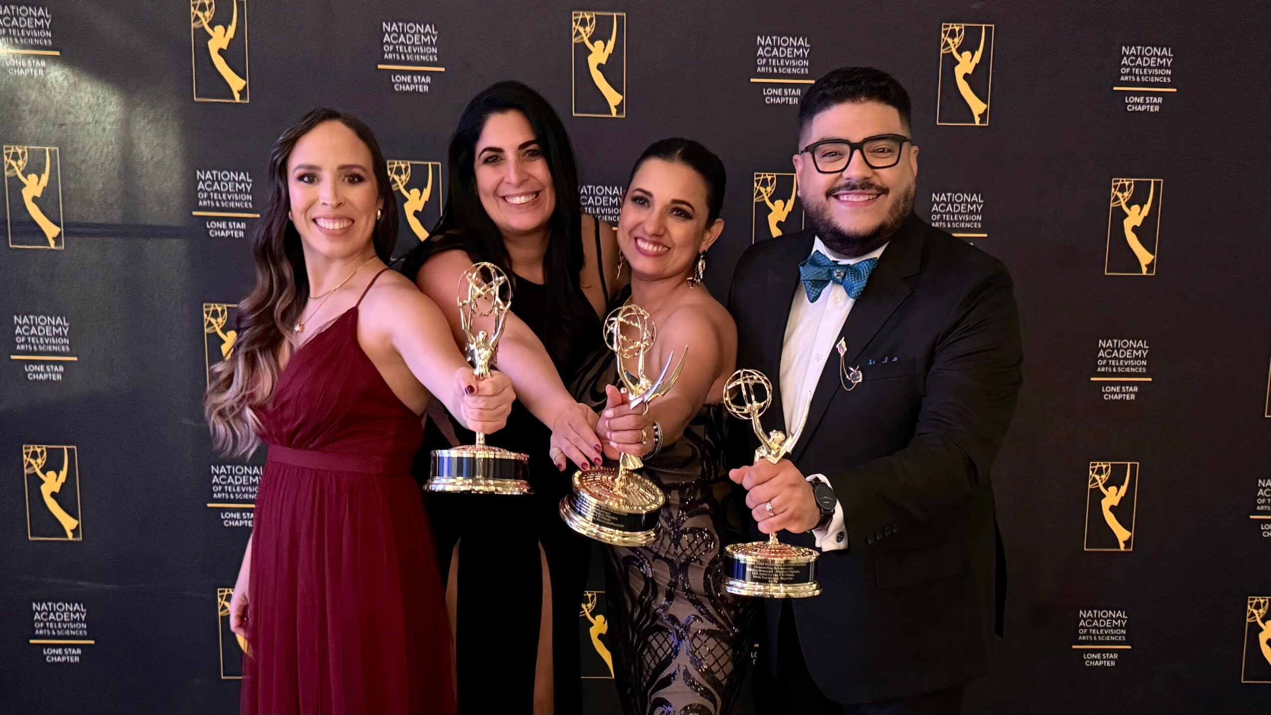 Four people holding awards and smiling at a formal event, with a black backdrop featuring logos.