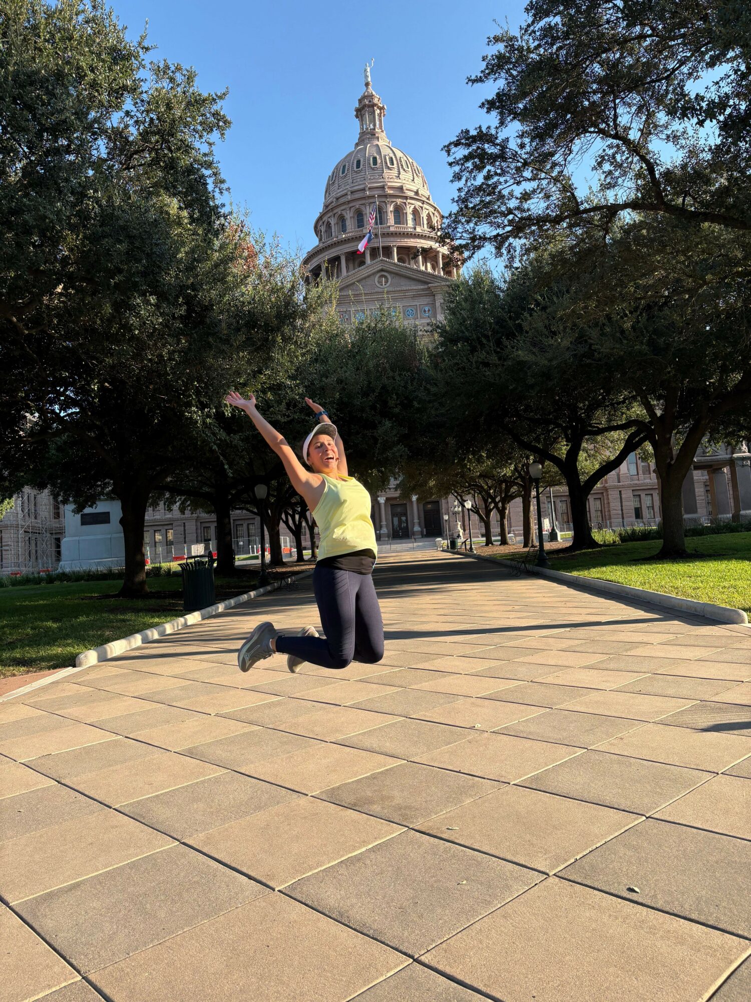 Person stretching outdoors on a paved walkway with trees and a building in the background.