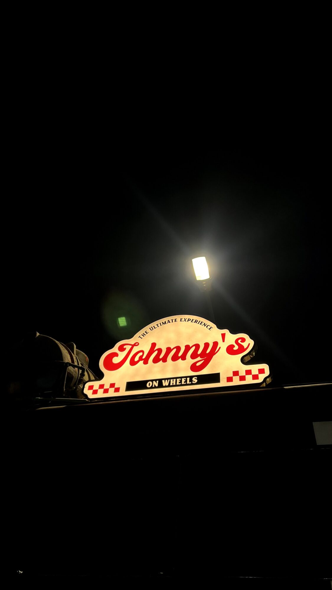 Nighttime scene with a lit sign reading 'Johnny's' and a streetlamp above, dark background.