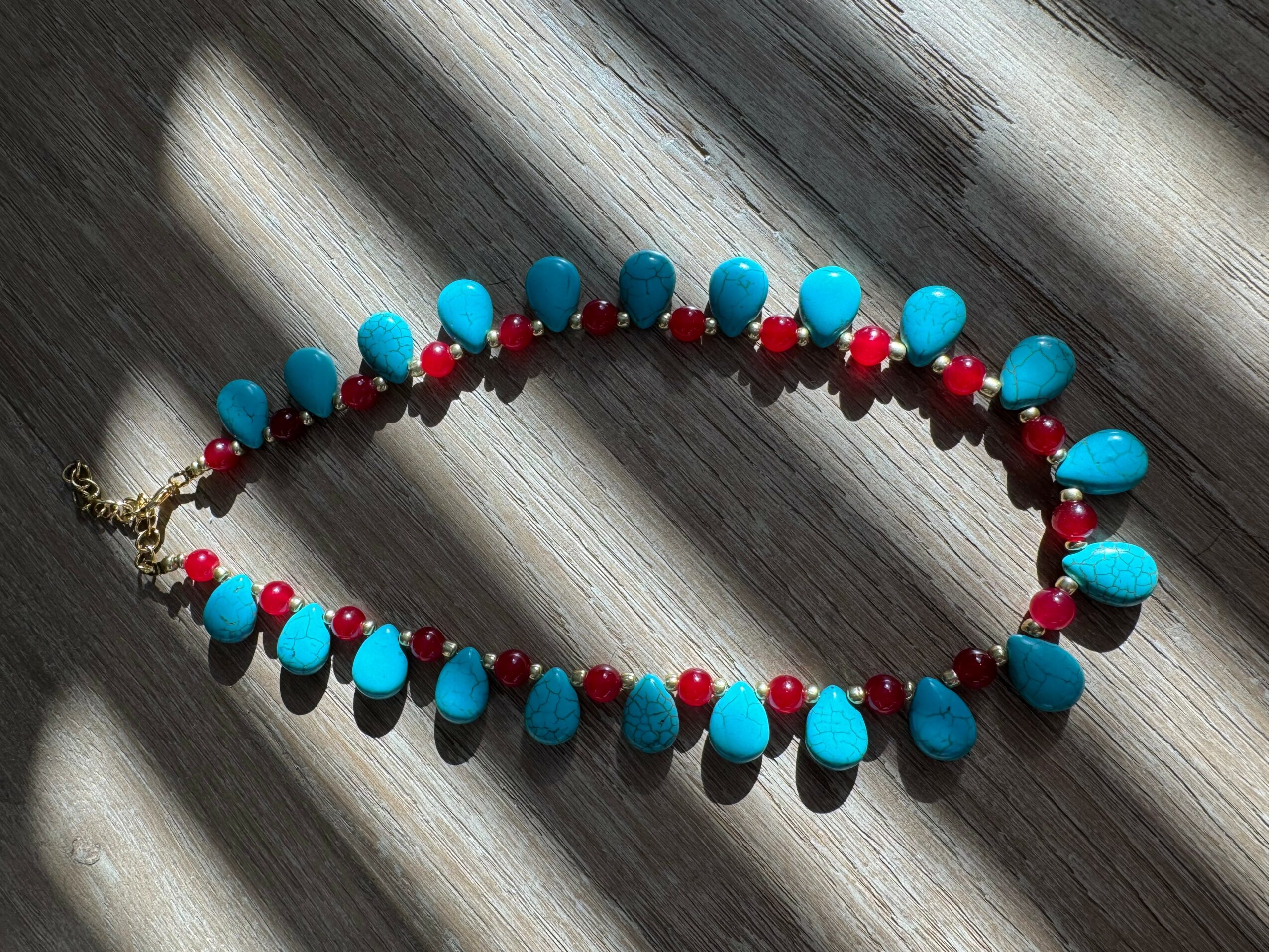 Necklace with blue and red beads on a wooden surface, sunlight casting shadows.