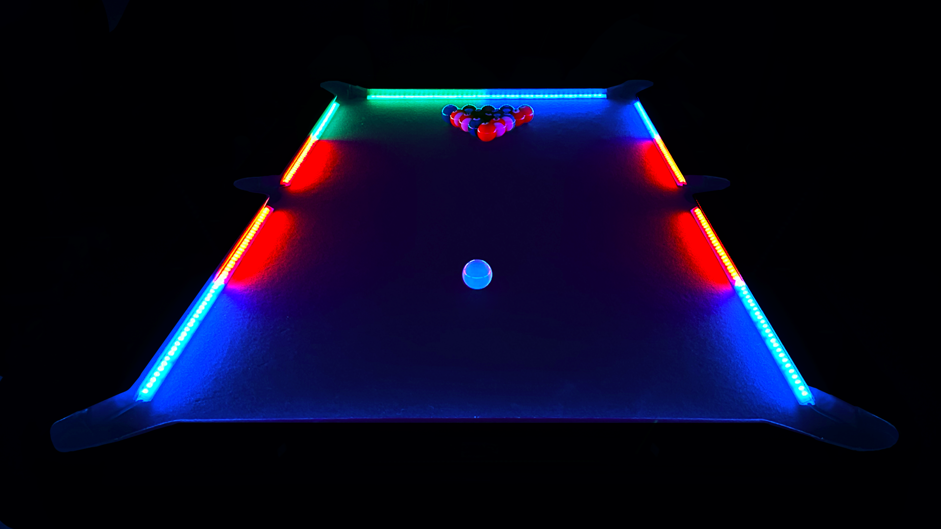 Colorful illuminated air hockey table with paddles and puck, viewed from the side in a dark environment.