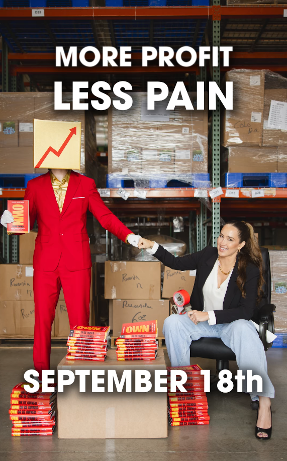 Two women in a warehouse, one in a red suit with a graph on her head, shaking hands, with boxes around.