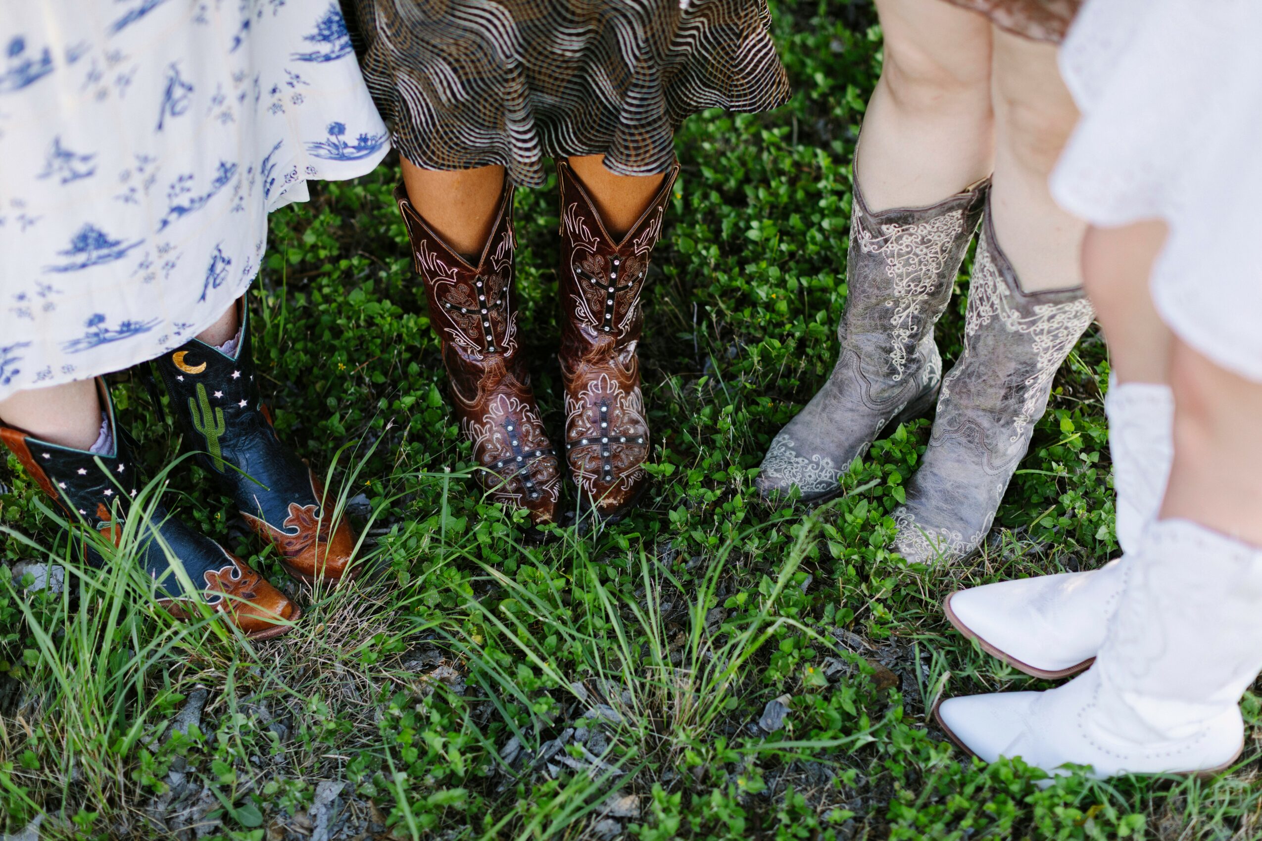 Group of children wearing cowboy boots standing on grass, with only their legs and boots visible.