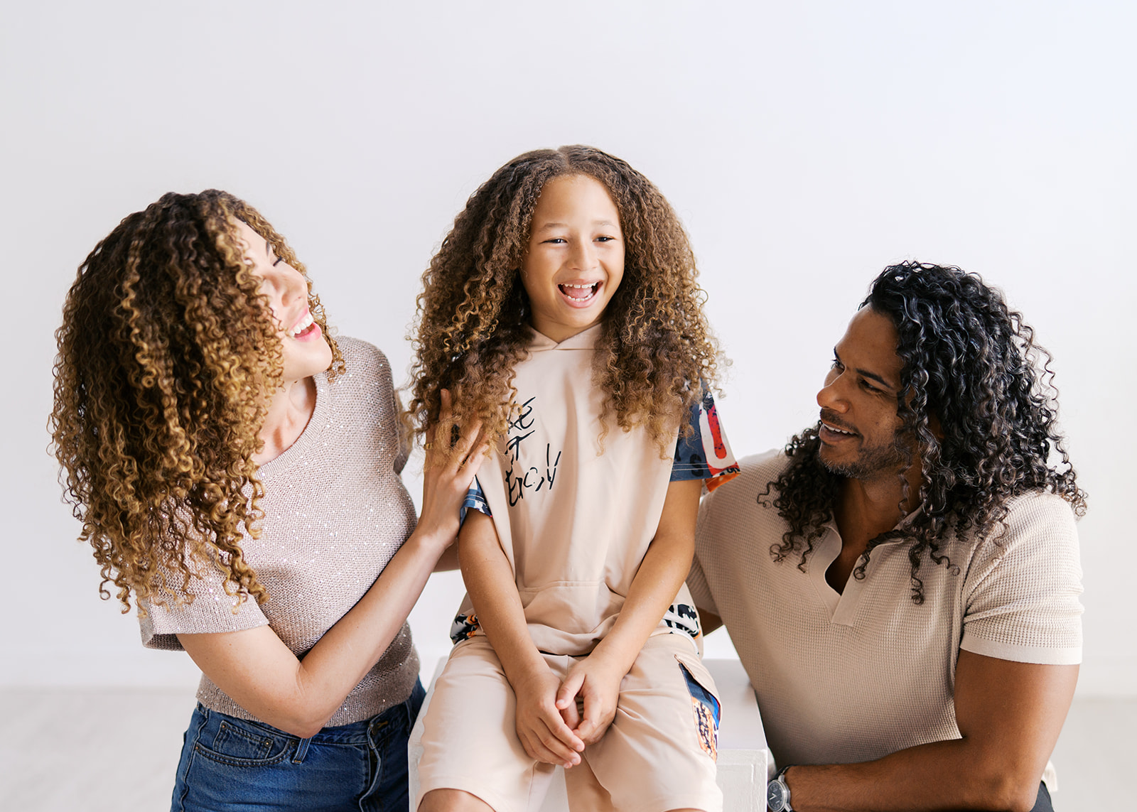 Two women and a girl sitting together, smiling and talking, in a bright room.