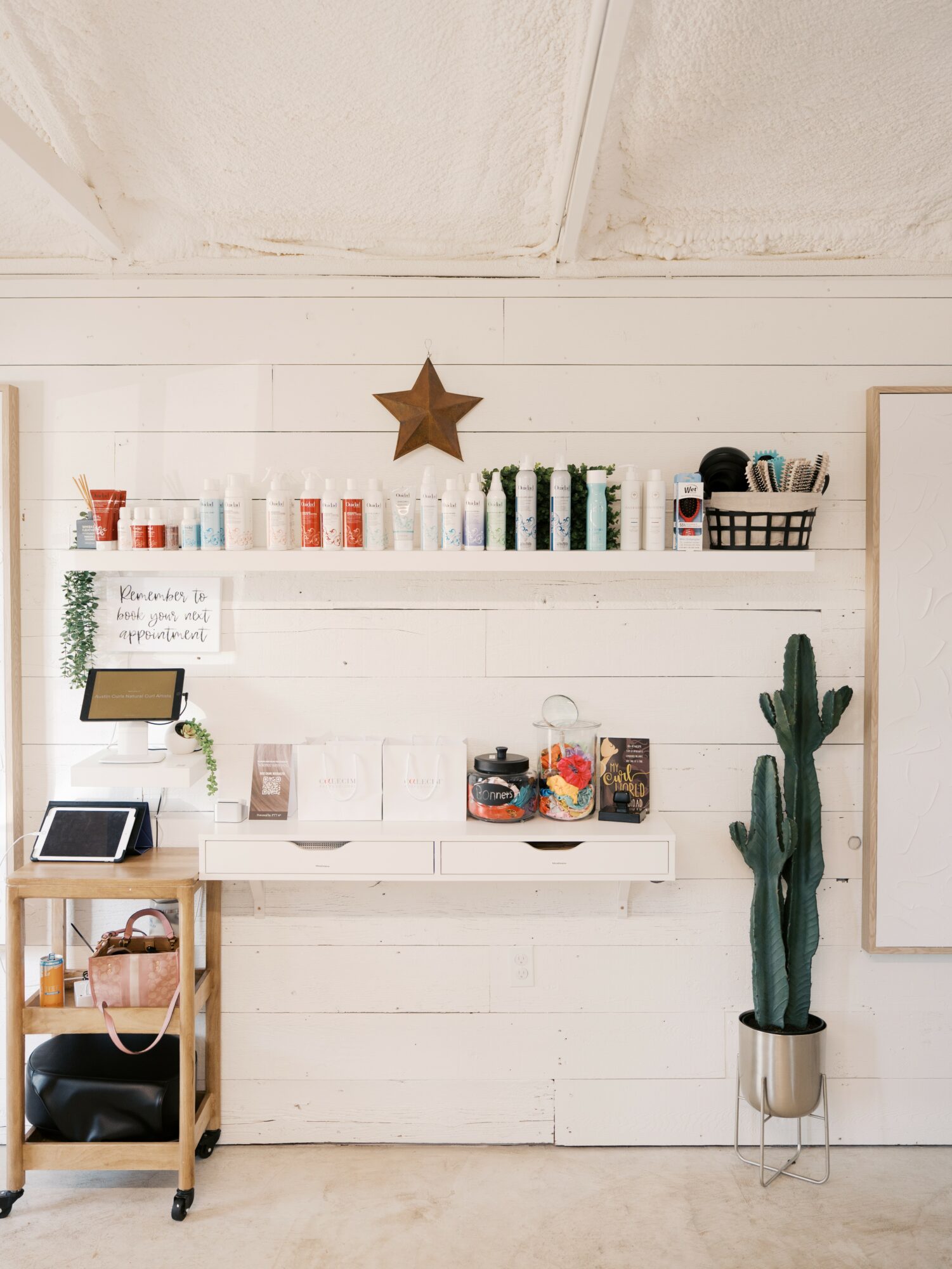 White wall with shelves holding colorful containers, a star decoration, a cactus plant, and a small cart with electronic devices.