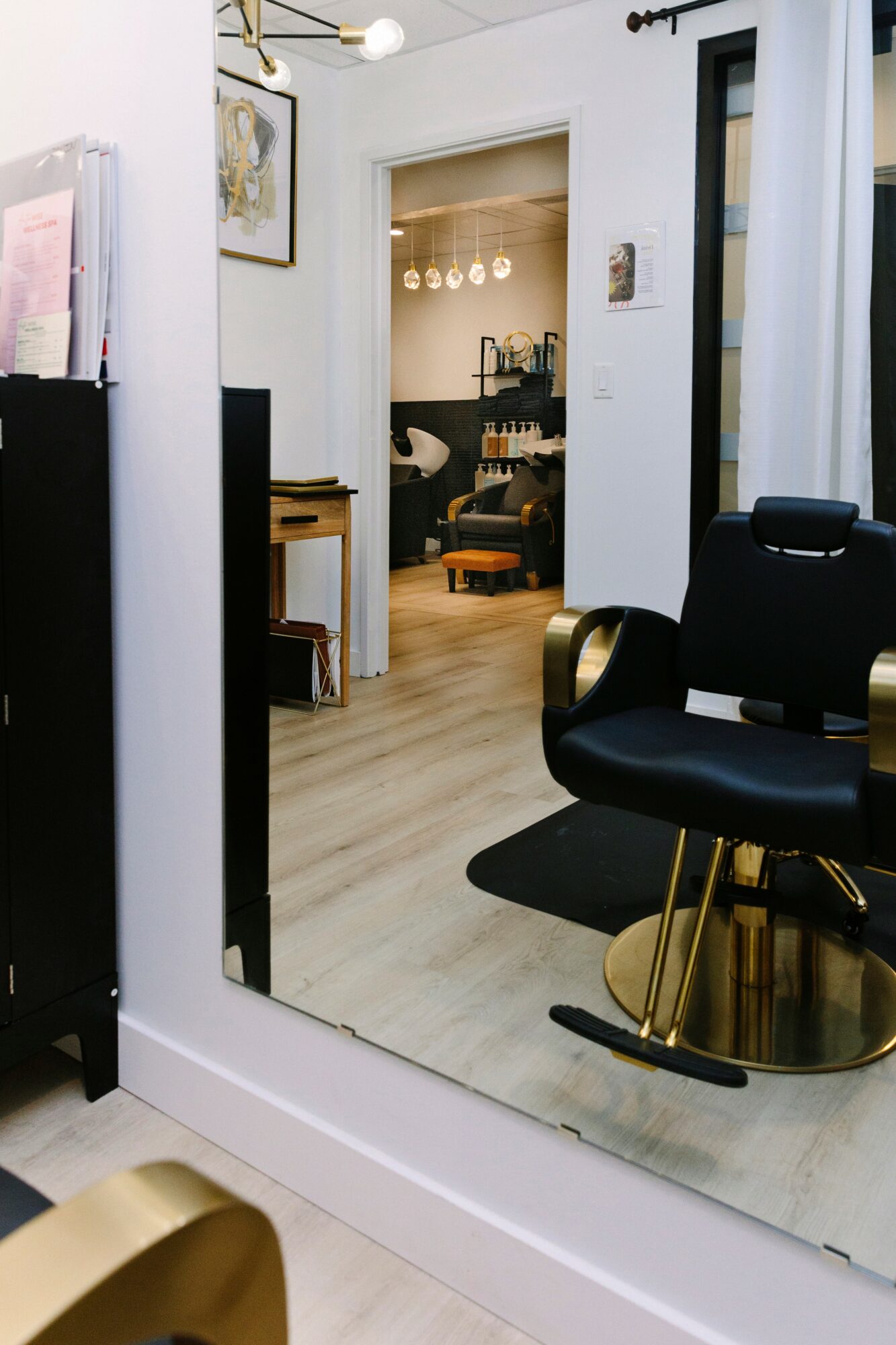 Salon chair reflected in a large mirror, with a room visible through an open doorway, modern decor, and wooden flooring.
