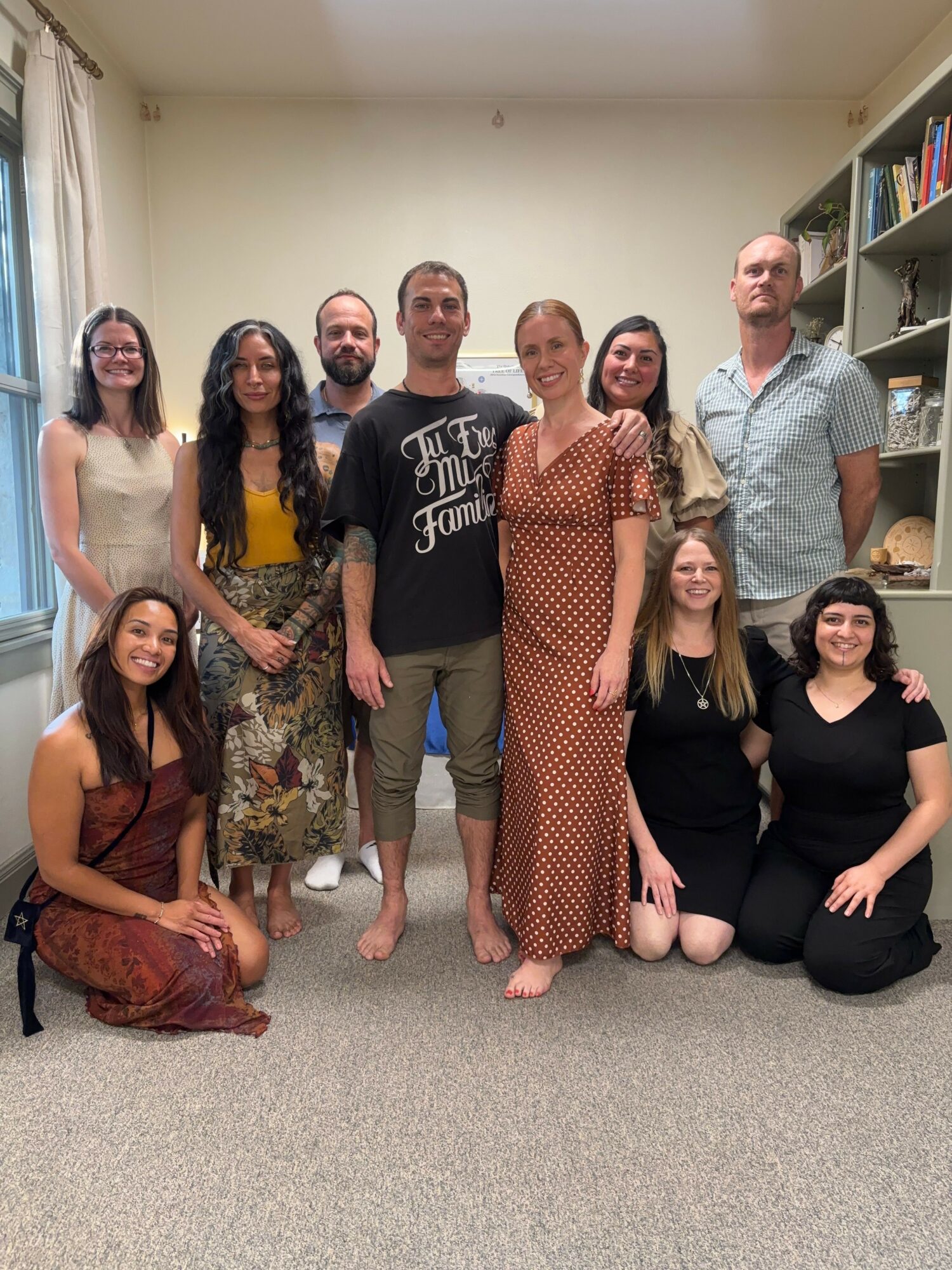 Group of nine people sitting and standing in a room with bookshelves, smiling at the camera.