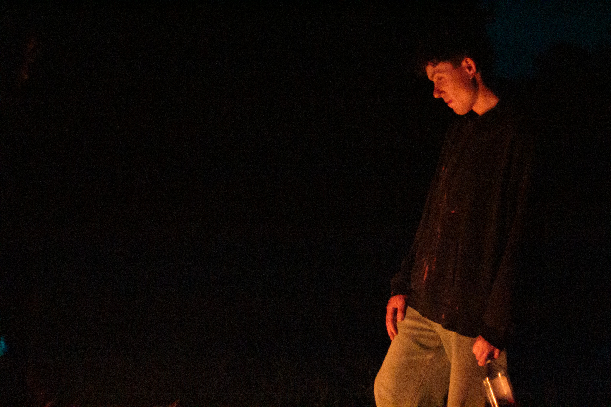 Person standing outdoors at night, looking down, holding an object, with dark background.