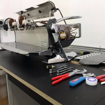 Disassembled machine parts on a black work surface with tools and screwdrivers nearby.