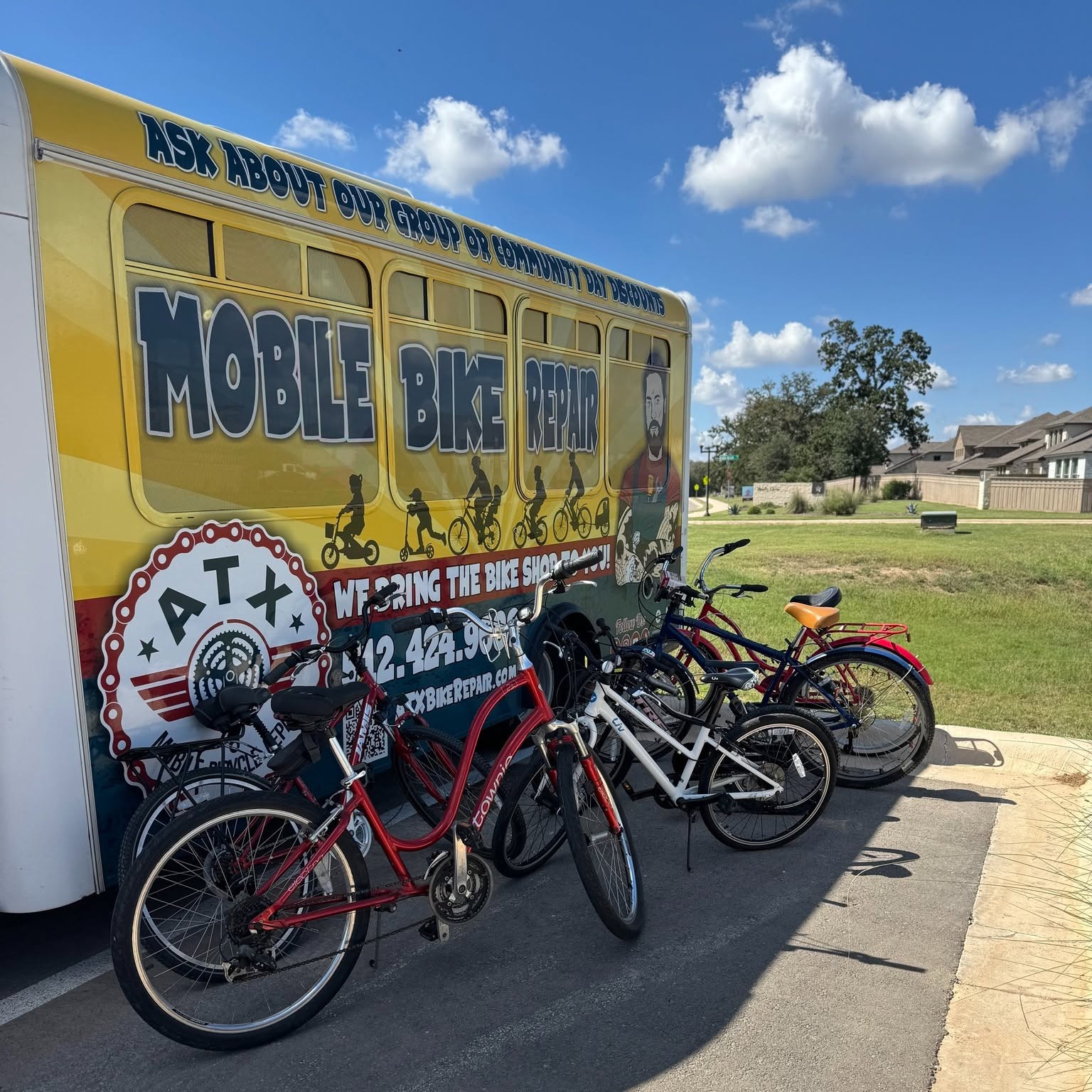 Four bicycles parked in front of a yellow mobile bike repair van on a sunny day with blue sky and clouds.