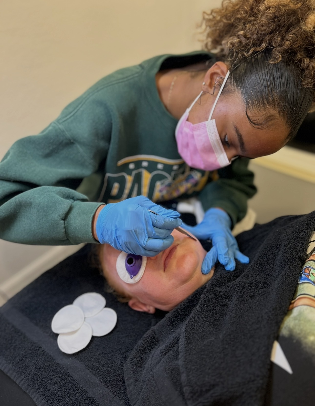 Healthcare worker wearing a pink mask and blue gloves examines a baby's mouth, who is lying down with a pacifier nearby.
