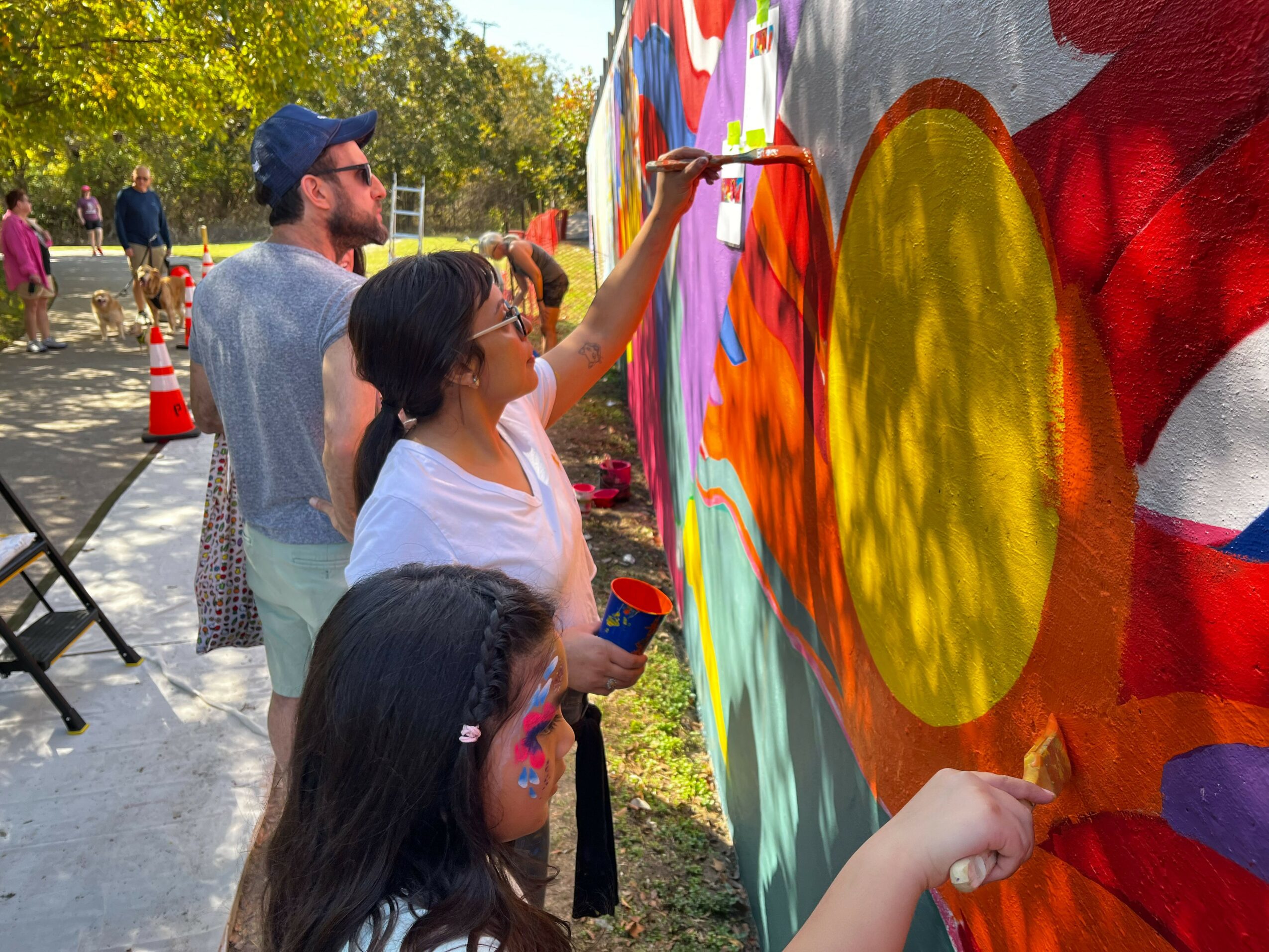 People painting a colorful mural outdoors with trees and traffic cones nearby.