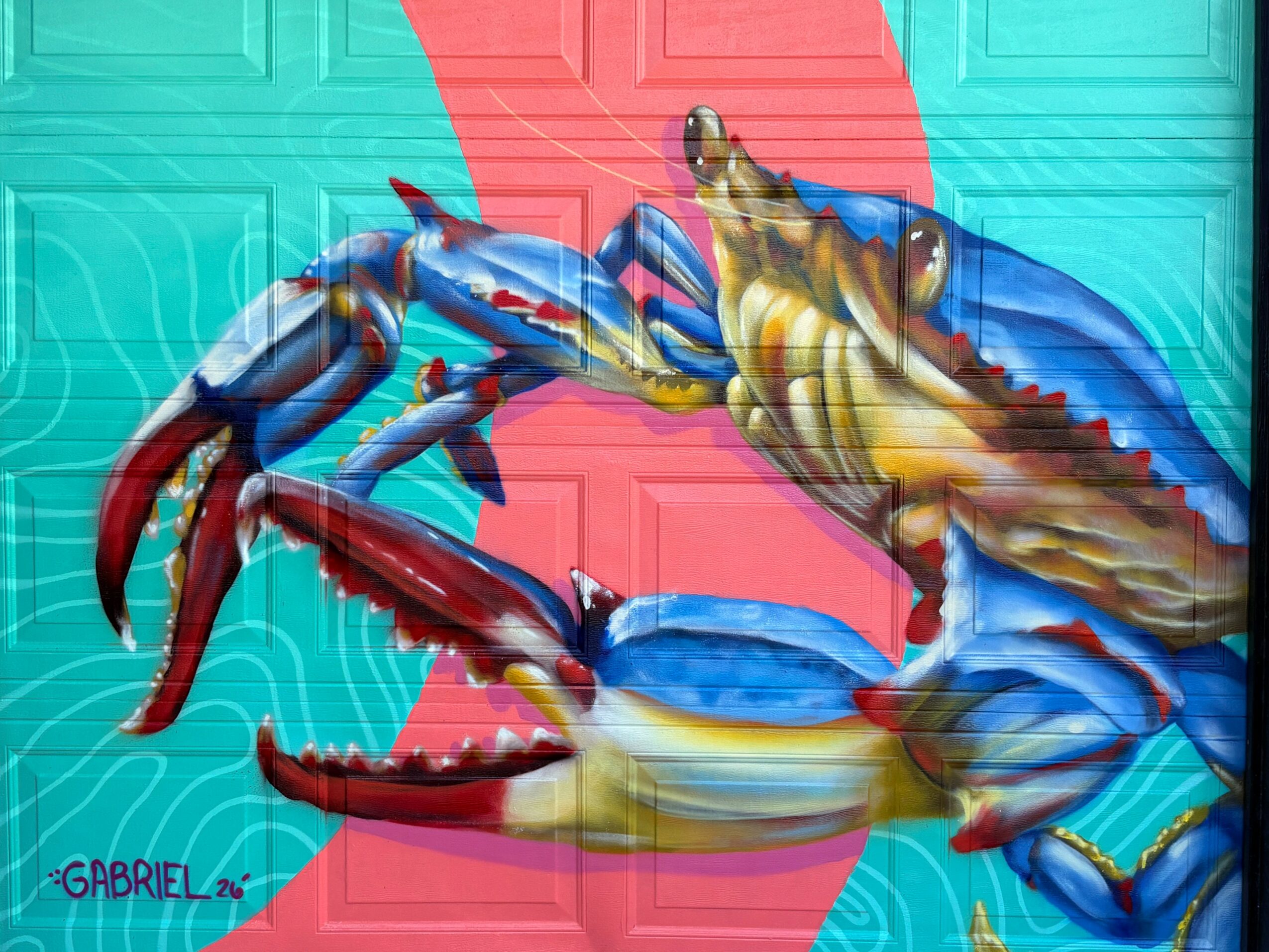 Colorful mural of a crab and a lobster on a wall with a pink background, signed 'GABRIEL 26'.