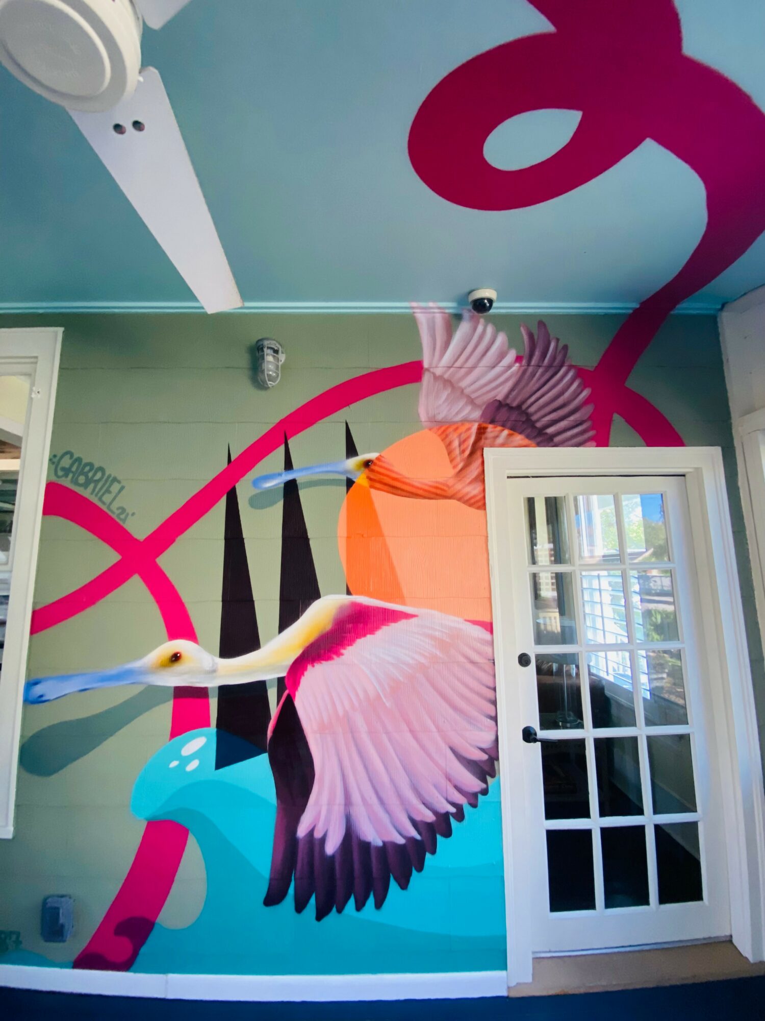 Colorful mural featuring a bird with pink, purple, and yellow feathers, and abstract shapes on a wall with a door.