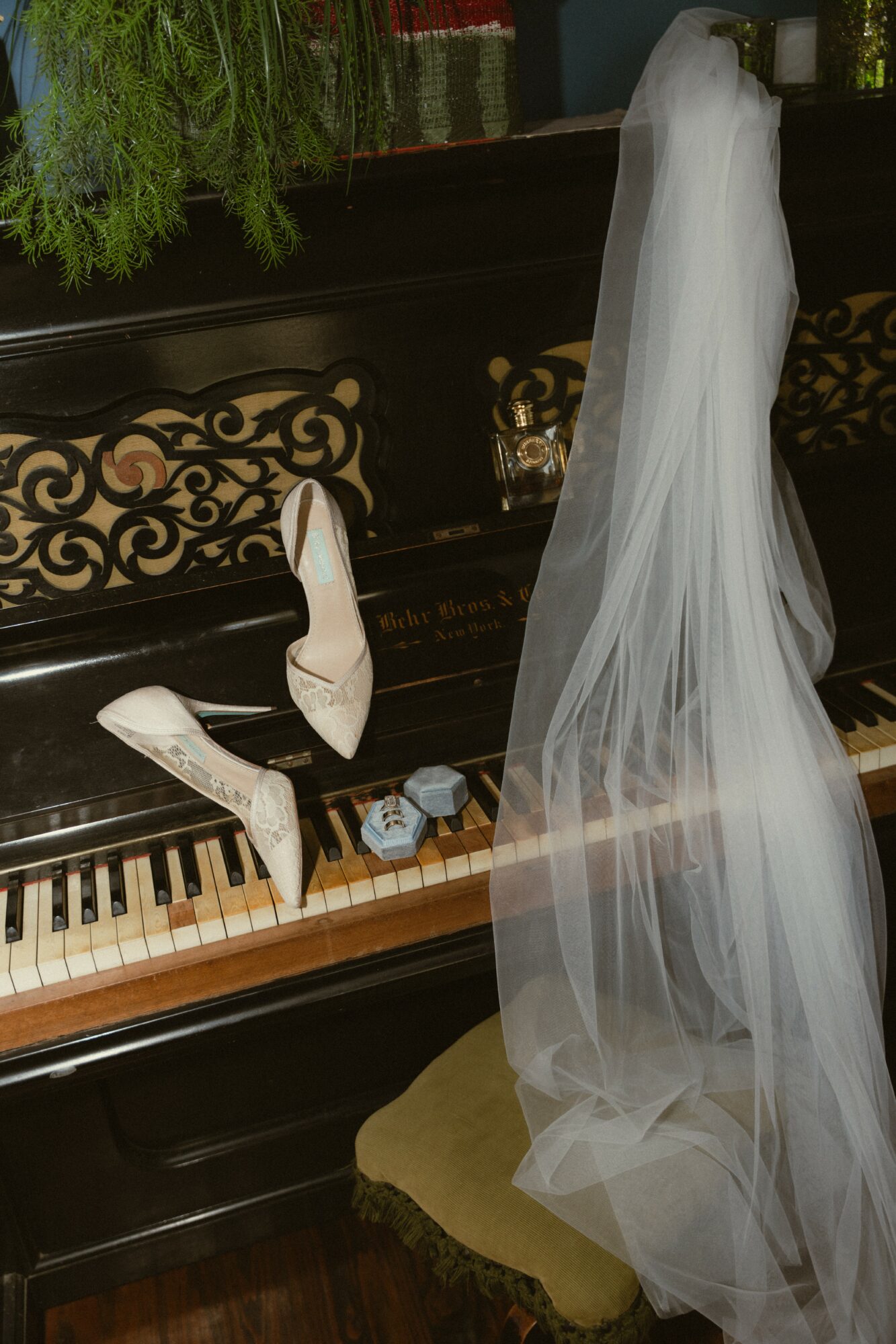 A piano with a white veil draped over it, a pair of white shoes, and a small box on the keys.