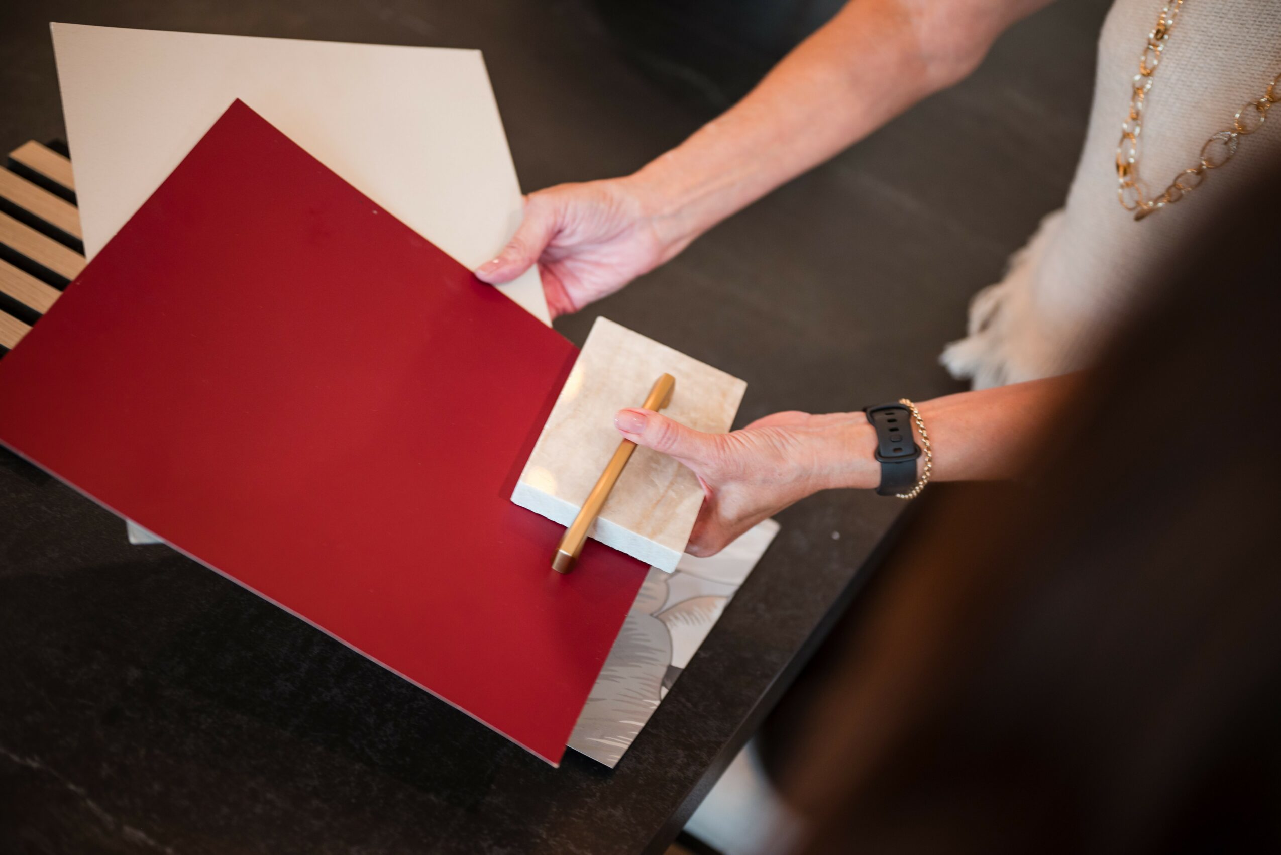 Person holding a red folder and a small white notepad with a pen, on a dark table.