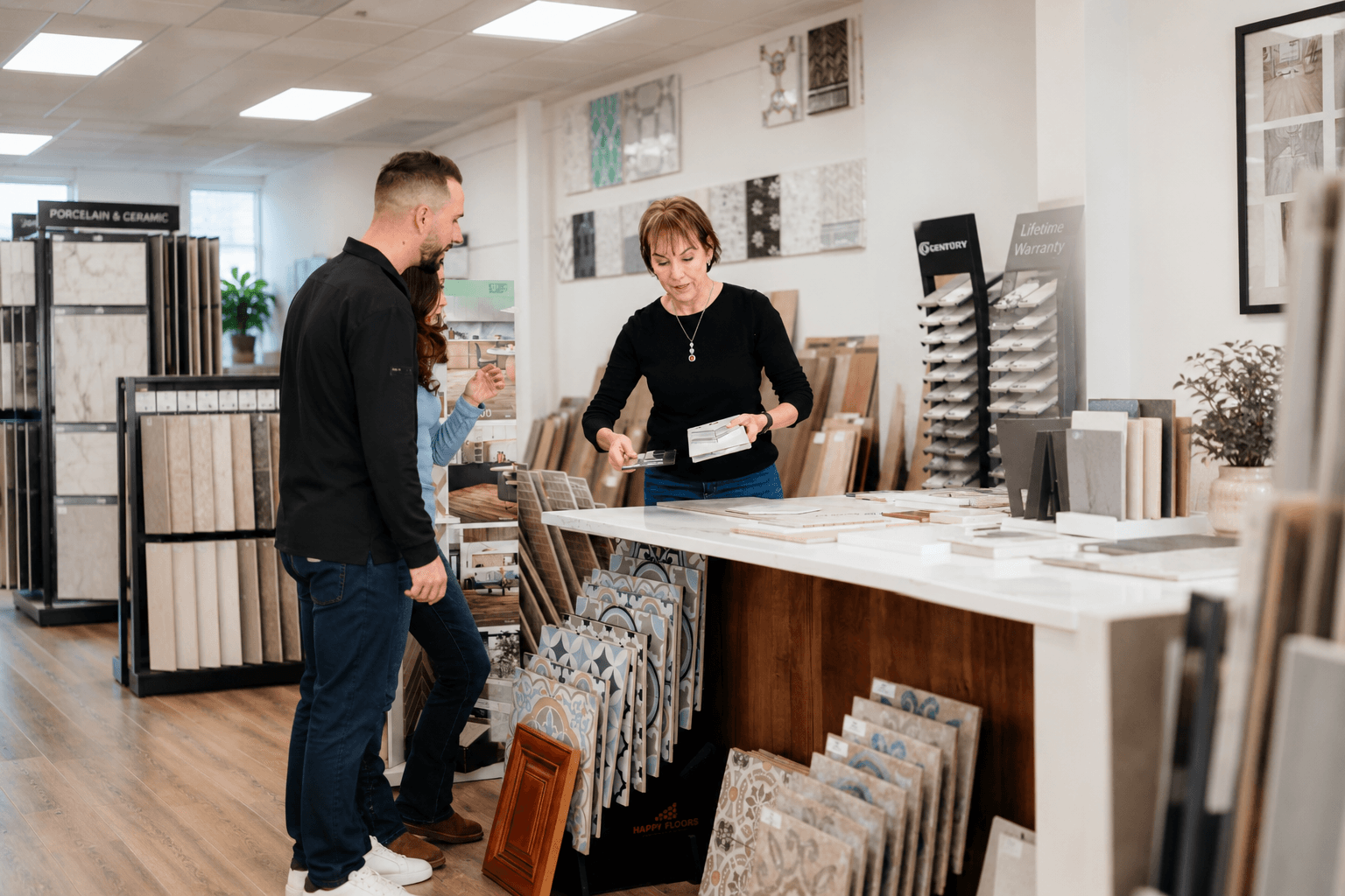 Person and customer talking in a tile and flooring store, with samples displayed on tables and shelves.