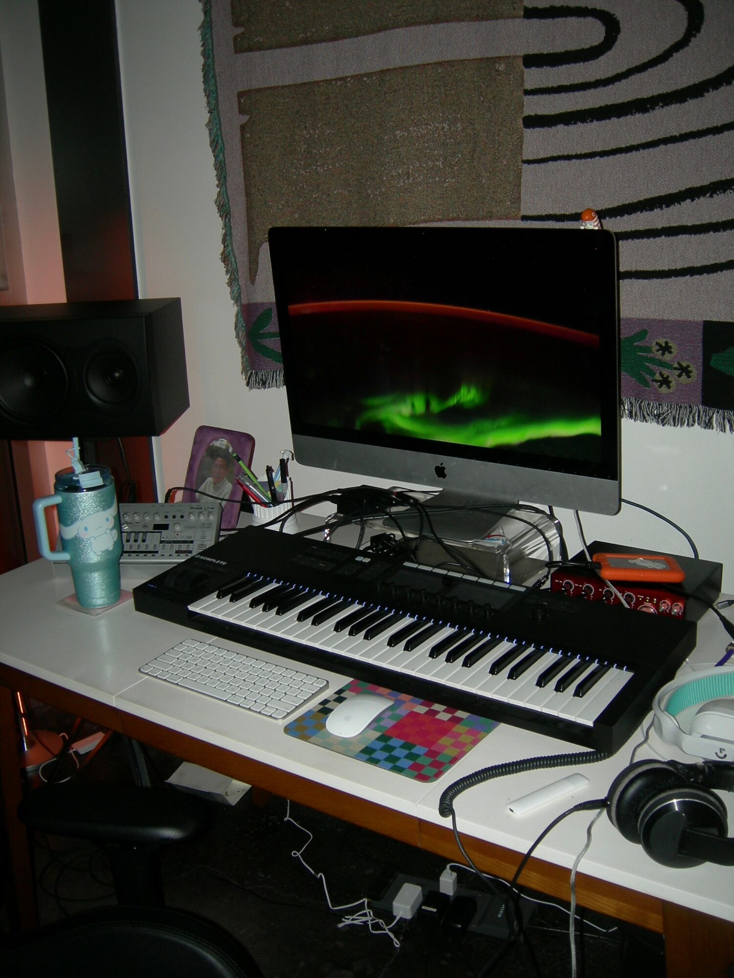 Music production setup with monitor, keyboard, speakers, and headphones on a desk.