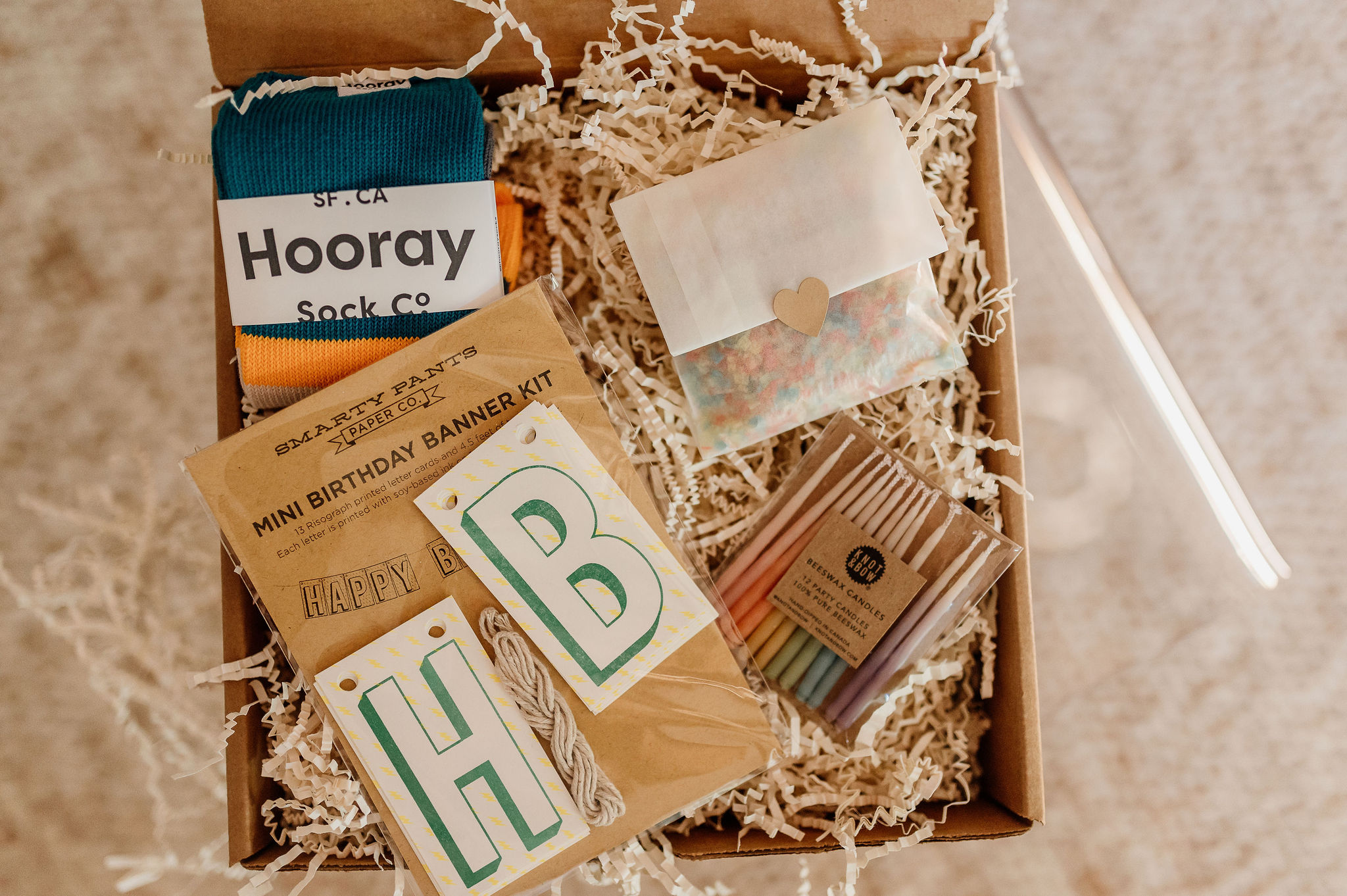 Open box with socks, cards, and paper, surrounded by shredded paper, on a beige surface.