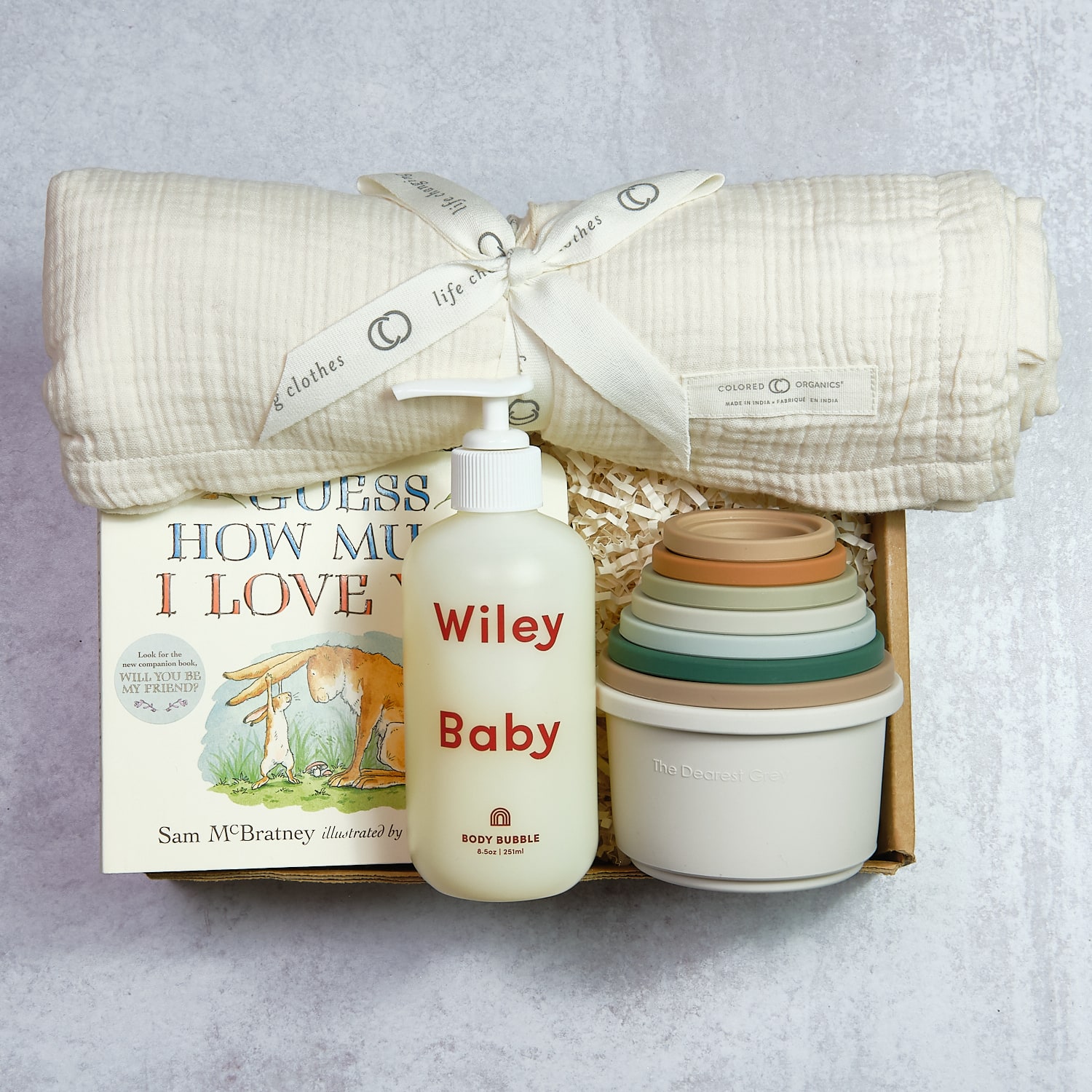 Baby blanket, bottle labeled 'Wiley Baby', and stack of bowls in a box, on a light surface.