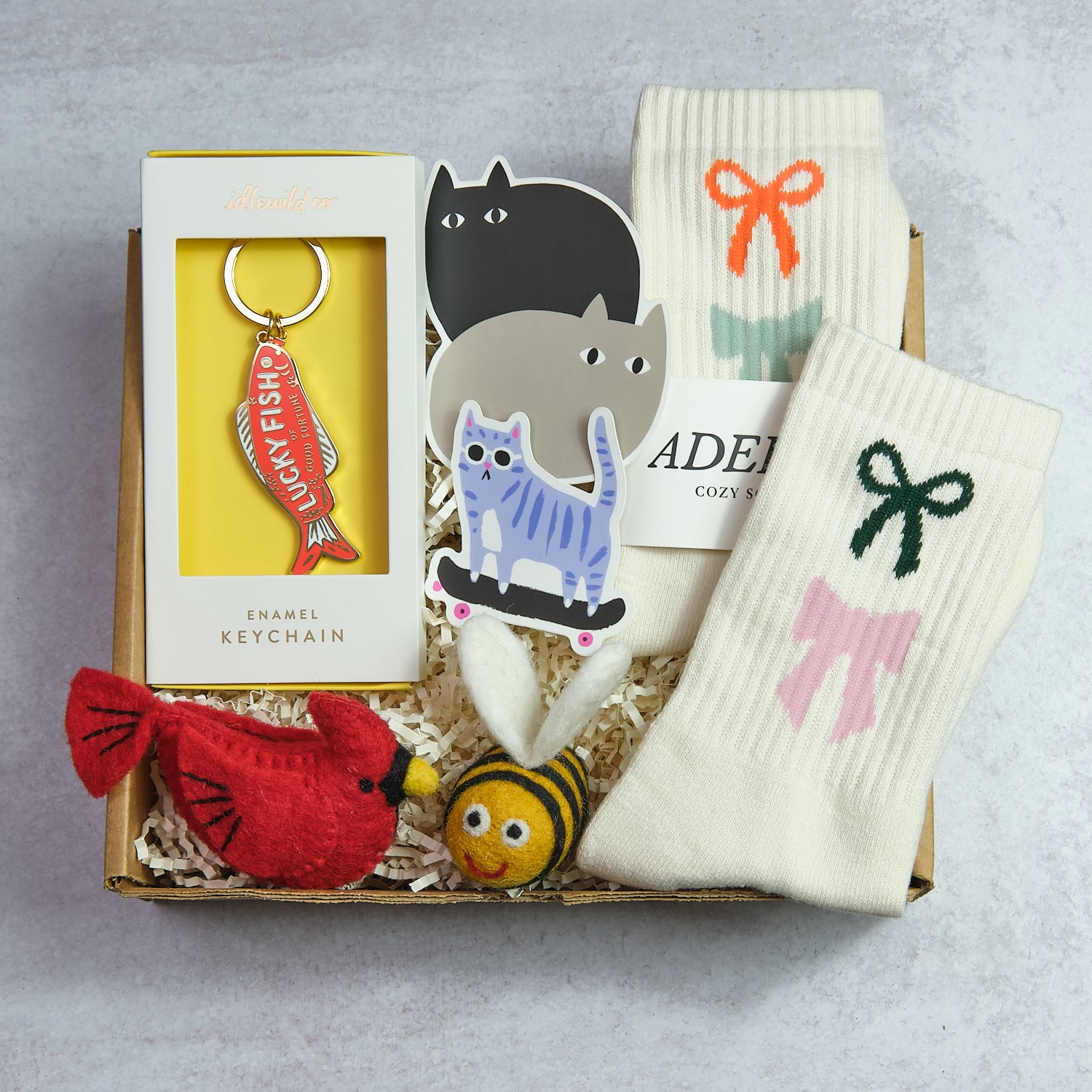 Gift box with socks, keychain, plush bird, bee, and cat stickers on a gray surface.