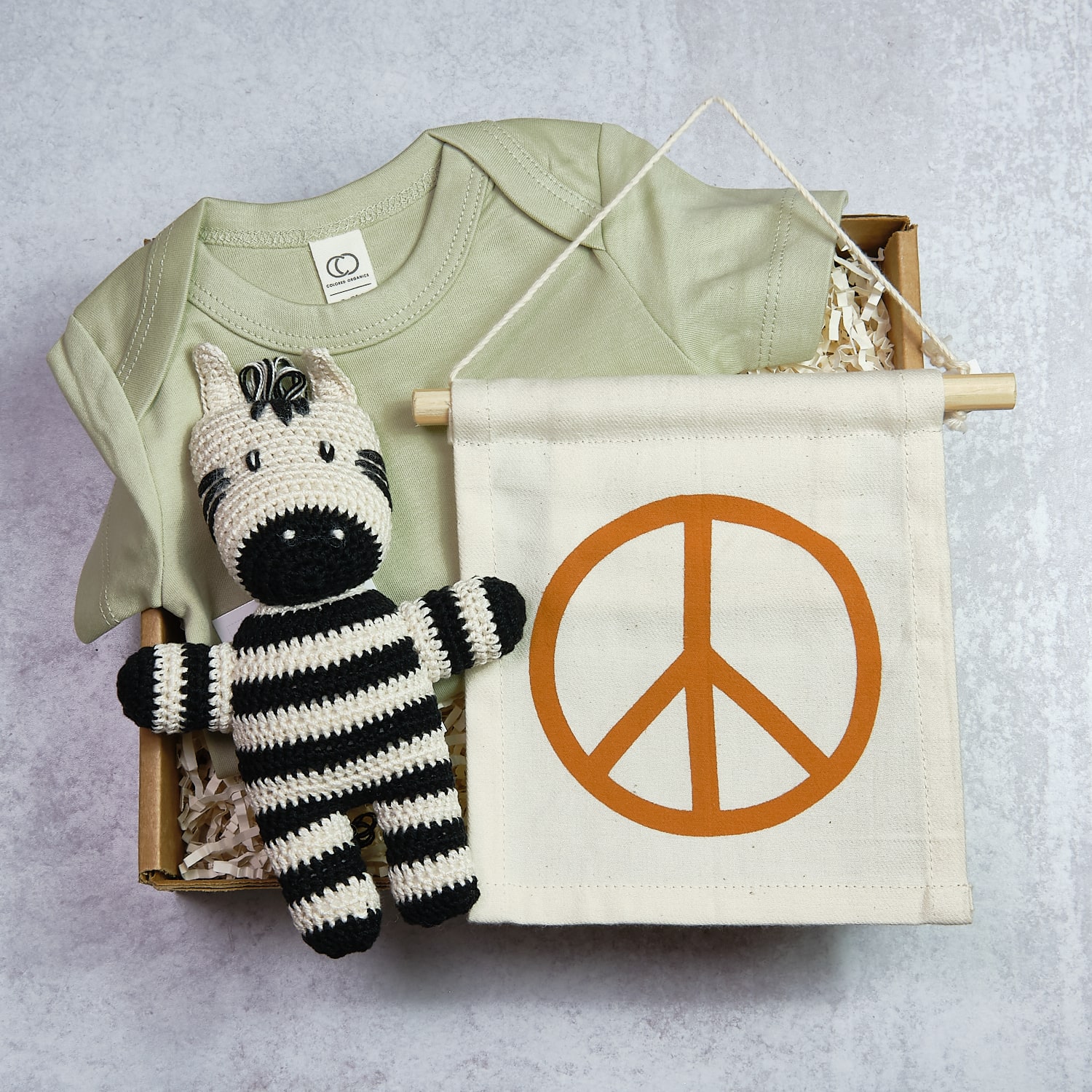 Baby clothes, a knitted zebra toy, and a peace sign banner on a gray background.