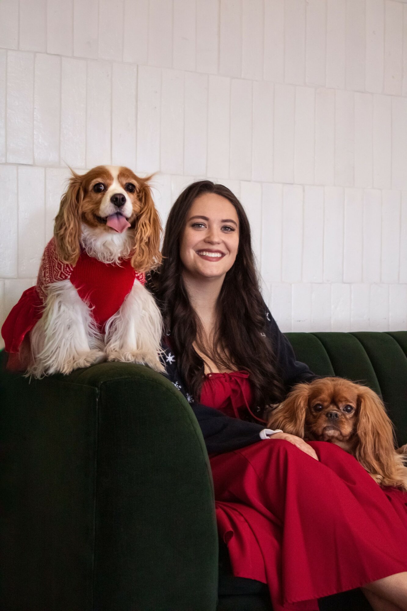 Woman sitting on a green couch with two dogs, one on her lap and one beside her, all smiling.