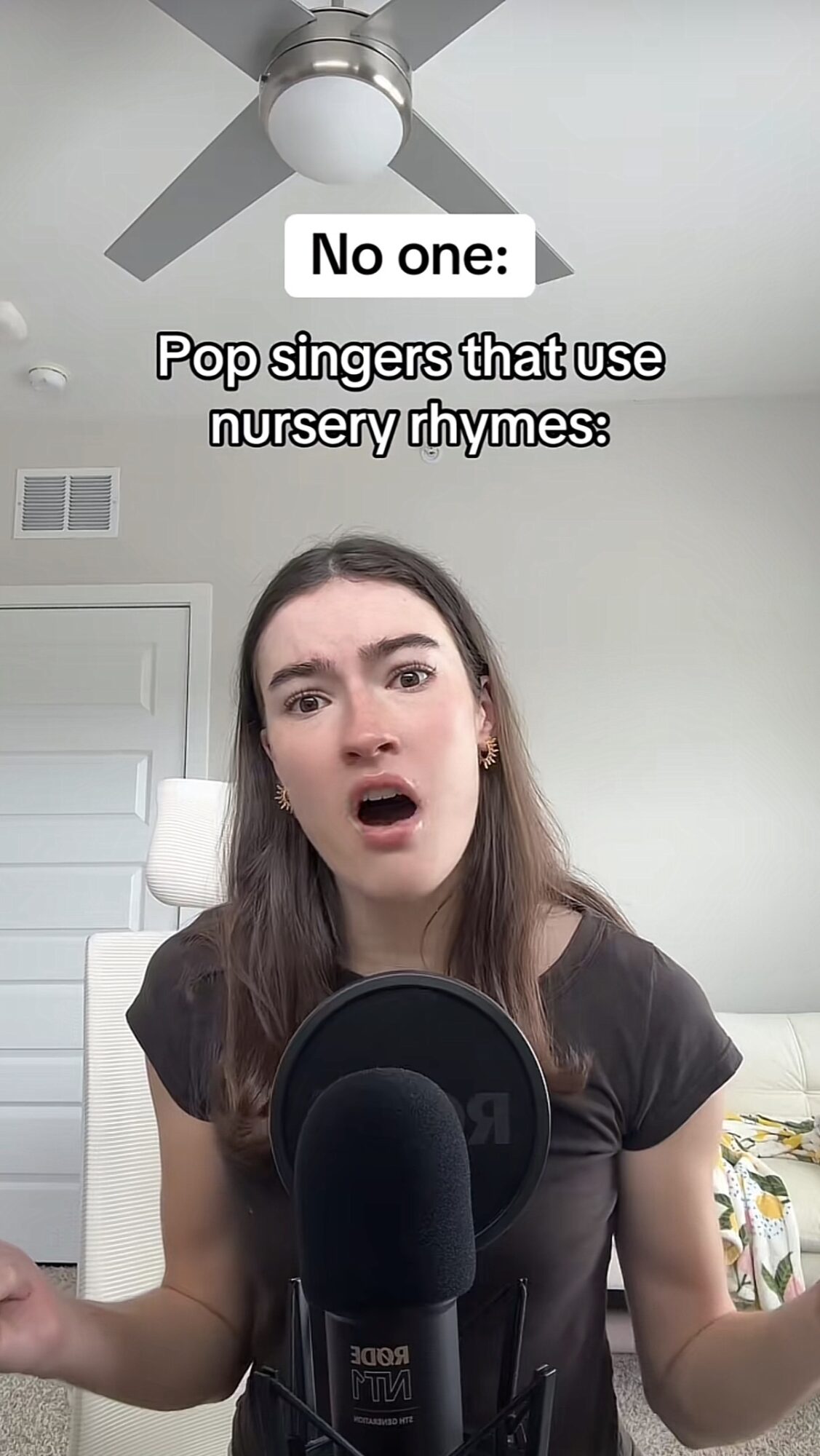Young woman with surprised expression in front of microphone, ceiling fan above, text overlay about nursery rhymes, neutral background.
