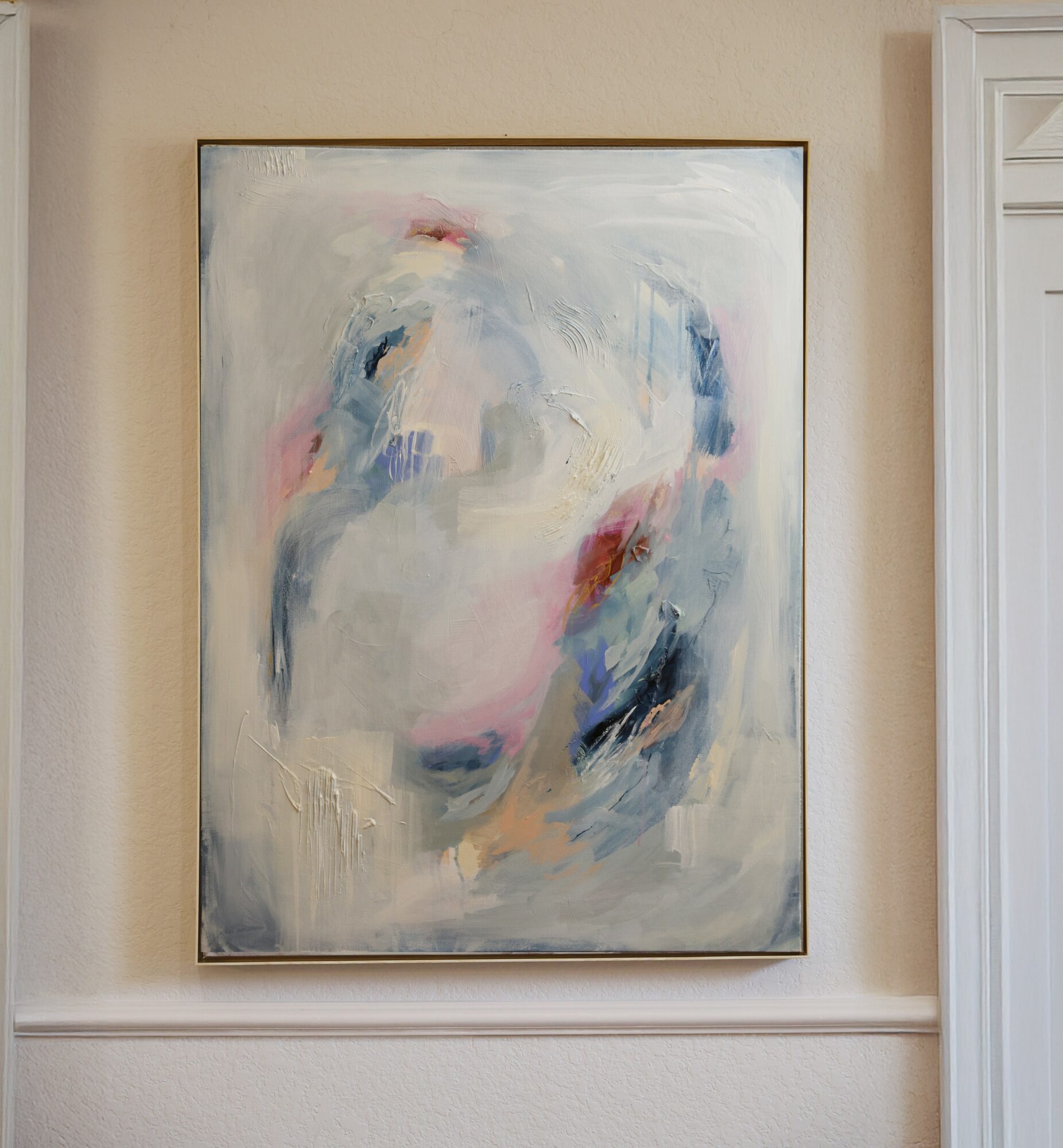 Abstract painting with soft pastel colors and brushstrokes on a beige wall.