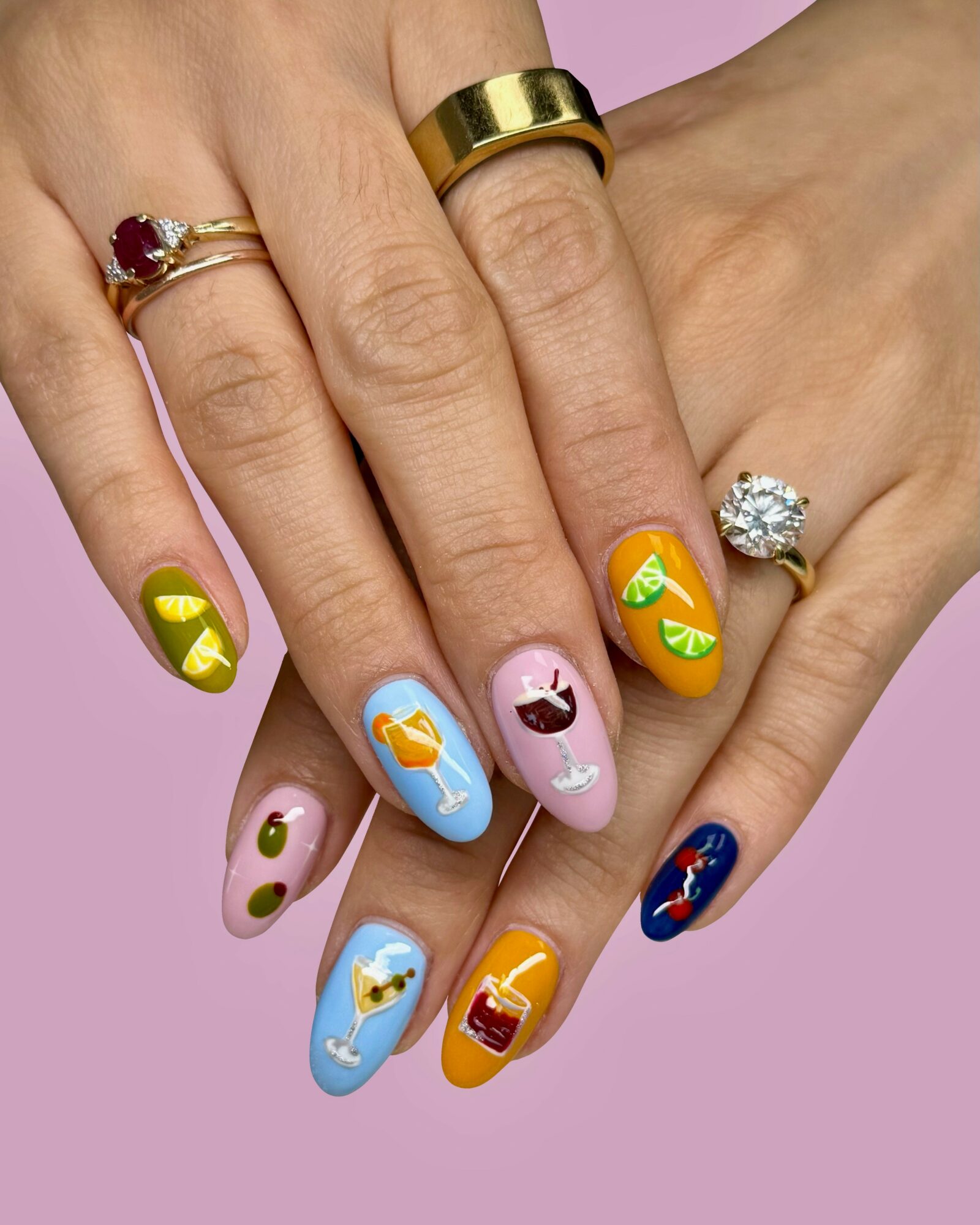 Two hands with colorful decorated nails and rings, against a pink background.