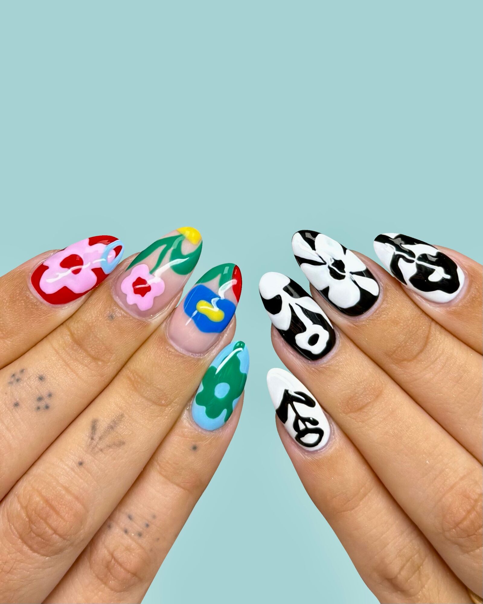 Two hands with colorful floral and abstract nail art against a light blue background.