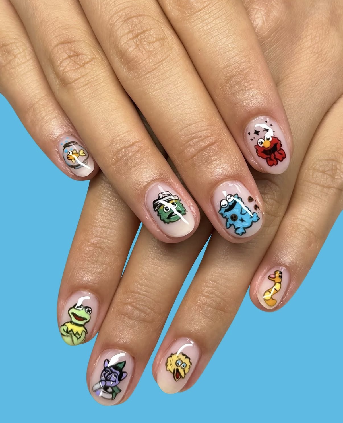 Hands with colorful cartoon character nail art on a blue background, featuring animals and playful designs.