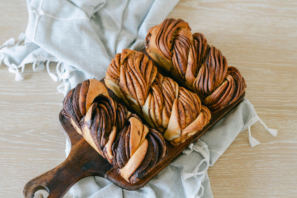 Four swirled pastries with chocolate and caramel on a wooden board, on a light cloth, on a wooden surface.