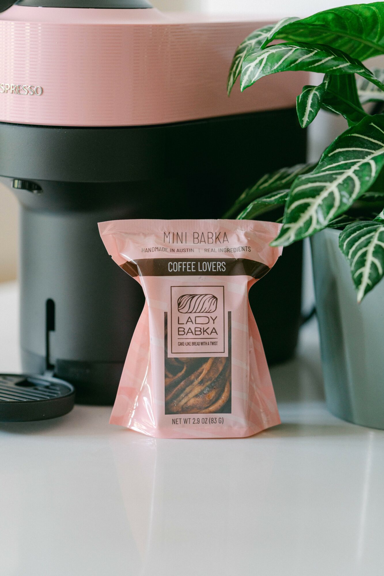 Coffee bag labeled 'Lady Baba' and 'Coffee Lovers' in front of a coffee machine and a potted plant.