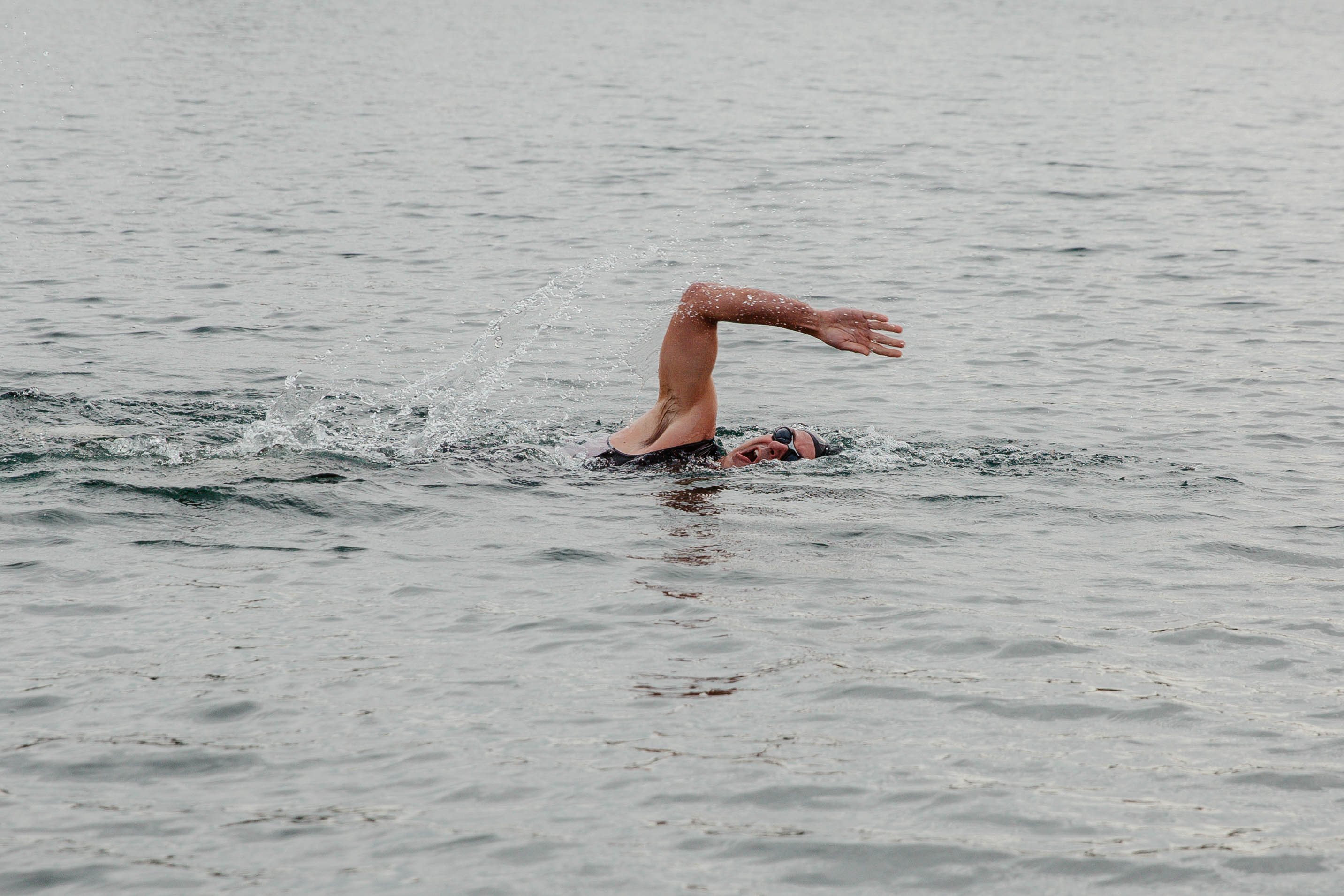 Person swimming in water with one arm raised above head, water ripples around them.
