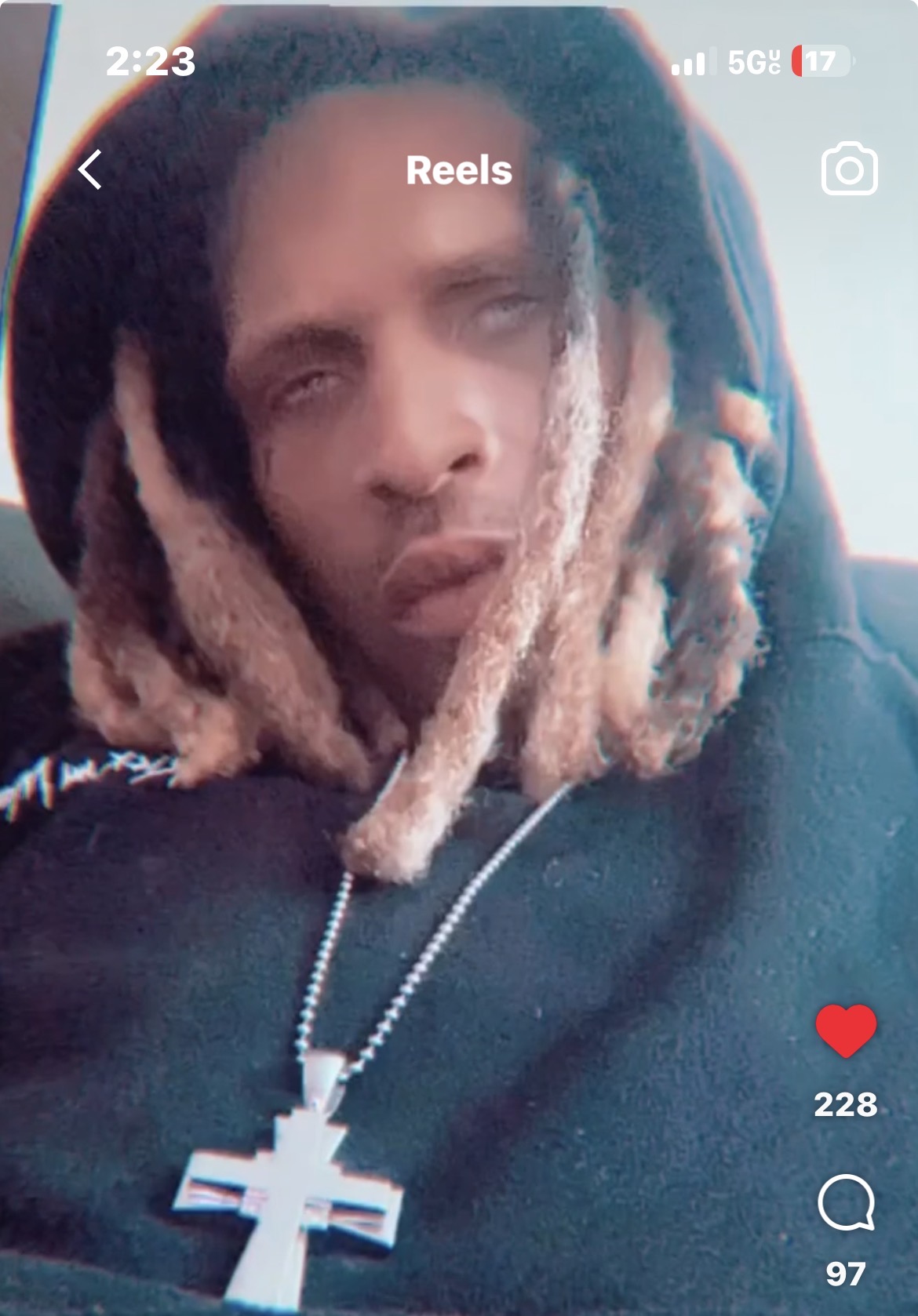 Person with dreadlocks wearing a cross necklace, looking at the camera, in a car.