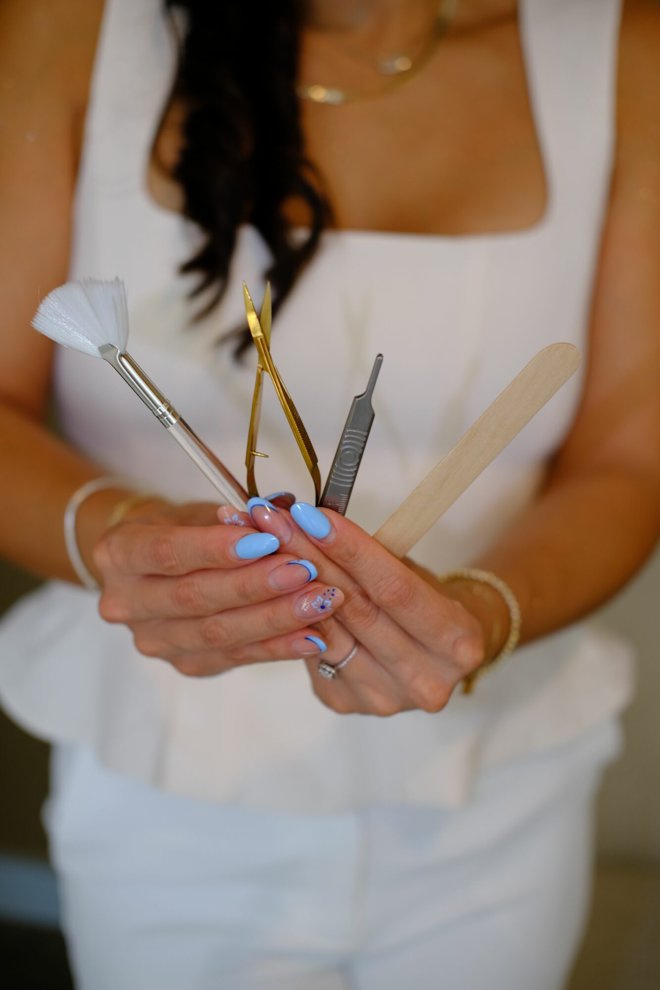 Close-up of a person's hand holding dental tools, with a woman lying down in the background, partially visible.