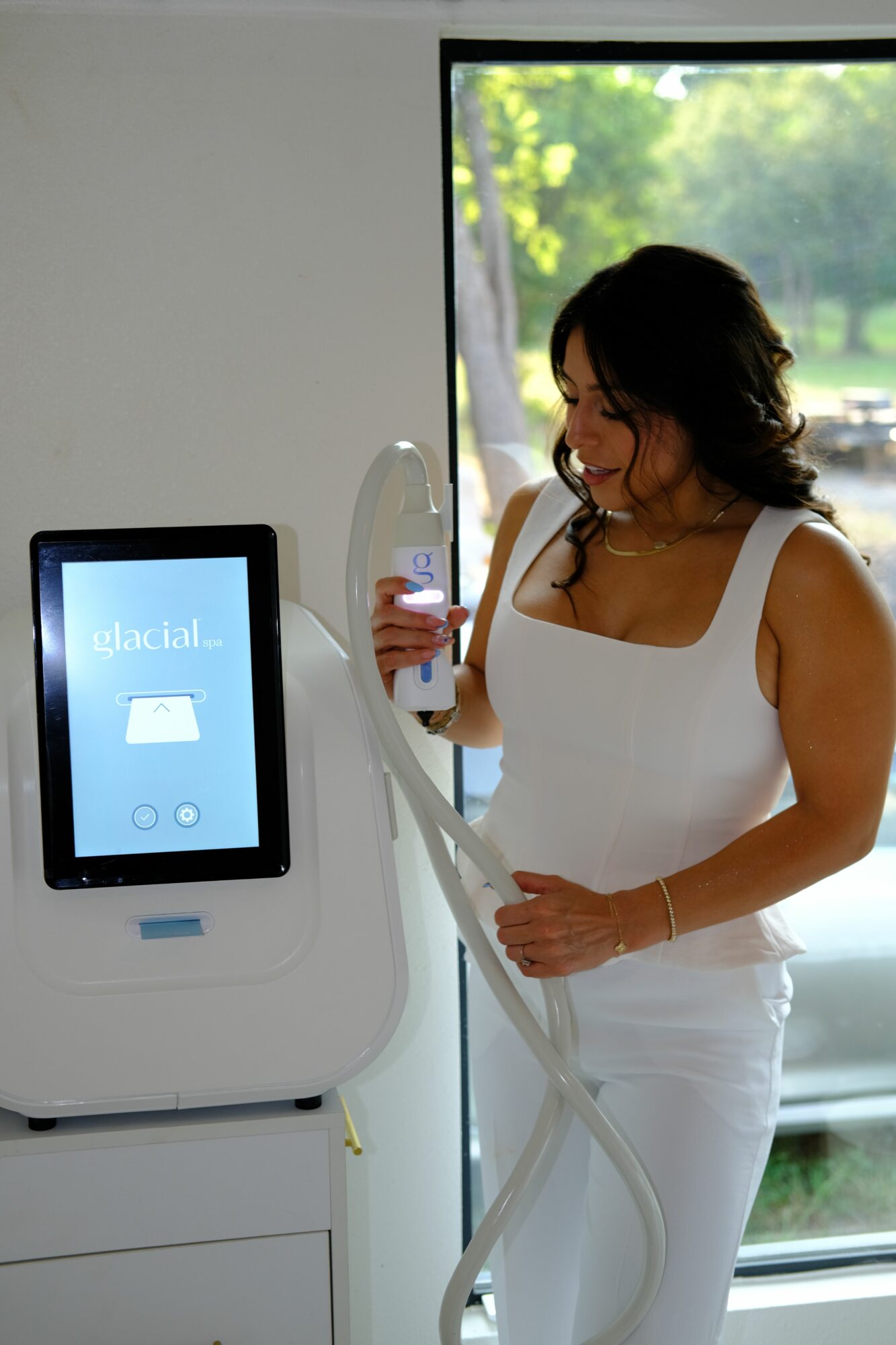 Woman in white dress taking a selfie in a medical imaging room with a large machine and a monitor.