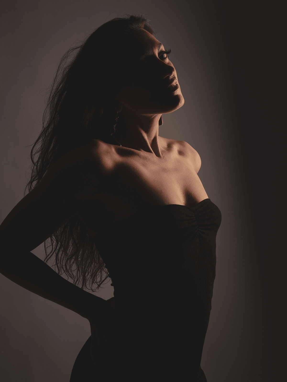 Silhouette of a woman with long hair, standing sideways with her head tilted upward, in a dark setting.