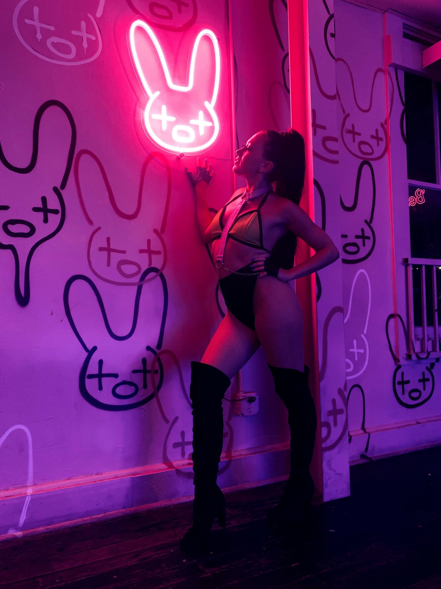 Person standing in front of a wall with neon bunny and abstract designs, illuminated by pink and purple lights.